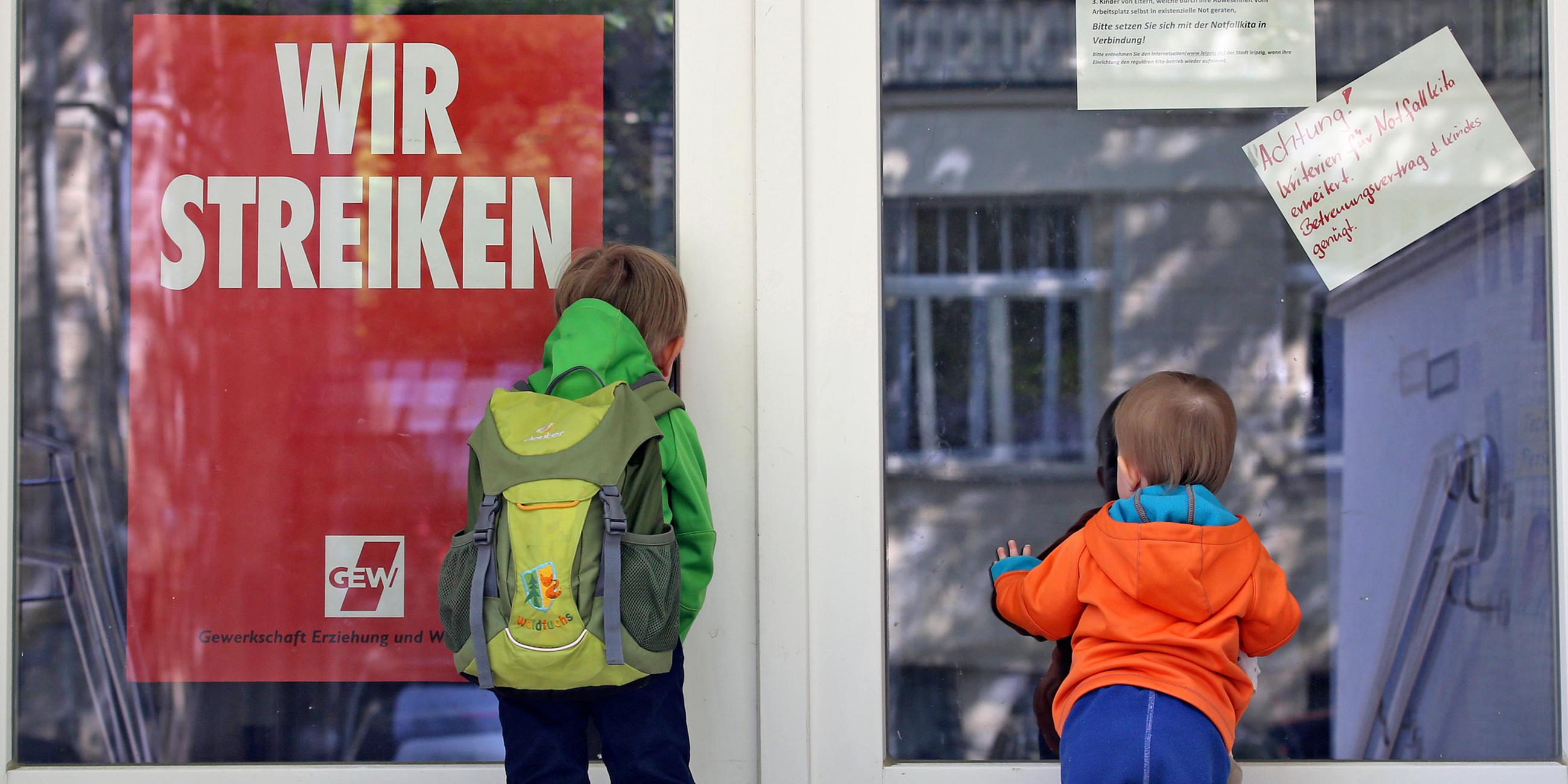 Zwei kleine Kinder stehen an der Tür eines wegen Streik geschlossenen Kindergartens