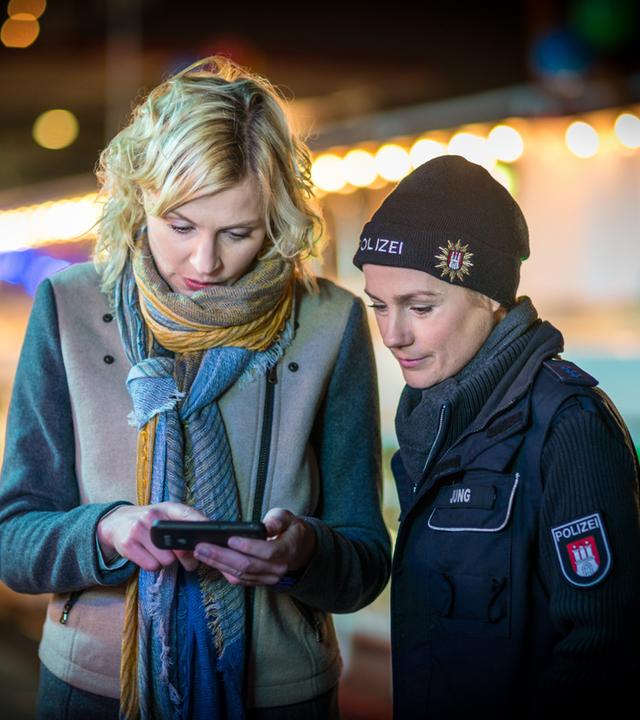 "Notruf Hafenkante - Klassentreffen": Die Polizeibeamtin Franzi Jung (Rhea Harder-Vennewald) steht neben Melanie Hansen (Sanna Englund) und schaut auf deren Handy, in dem Melanie ihr etwas zeigt.