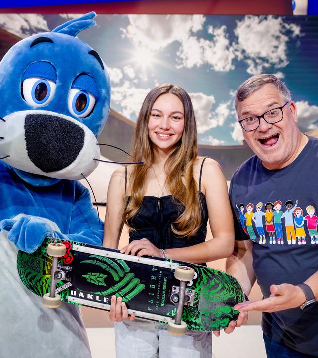 "1, 2 oder 3 - Kleine Helden, große Taten": Skaterin Lilly Stoephasius steht mit ihrem Skateboard in der Hand zwischen Piet Flosse und Elton im Studio.