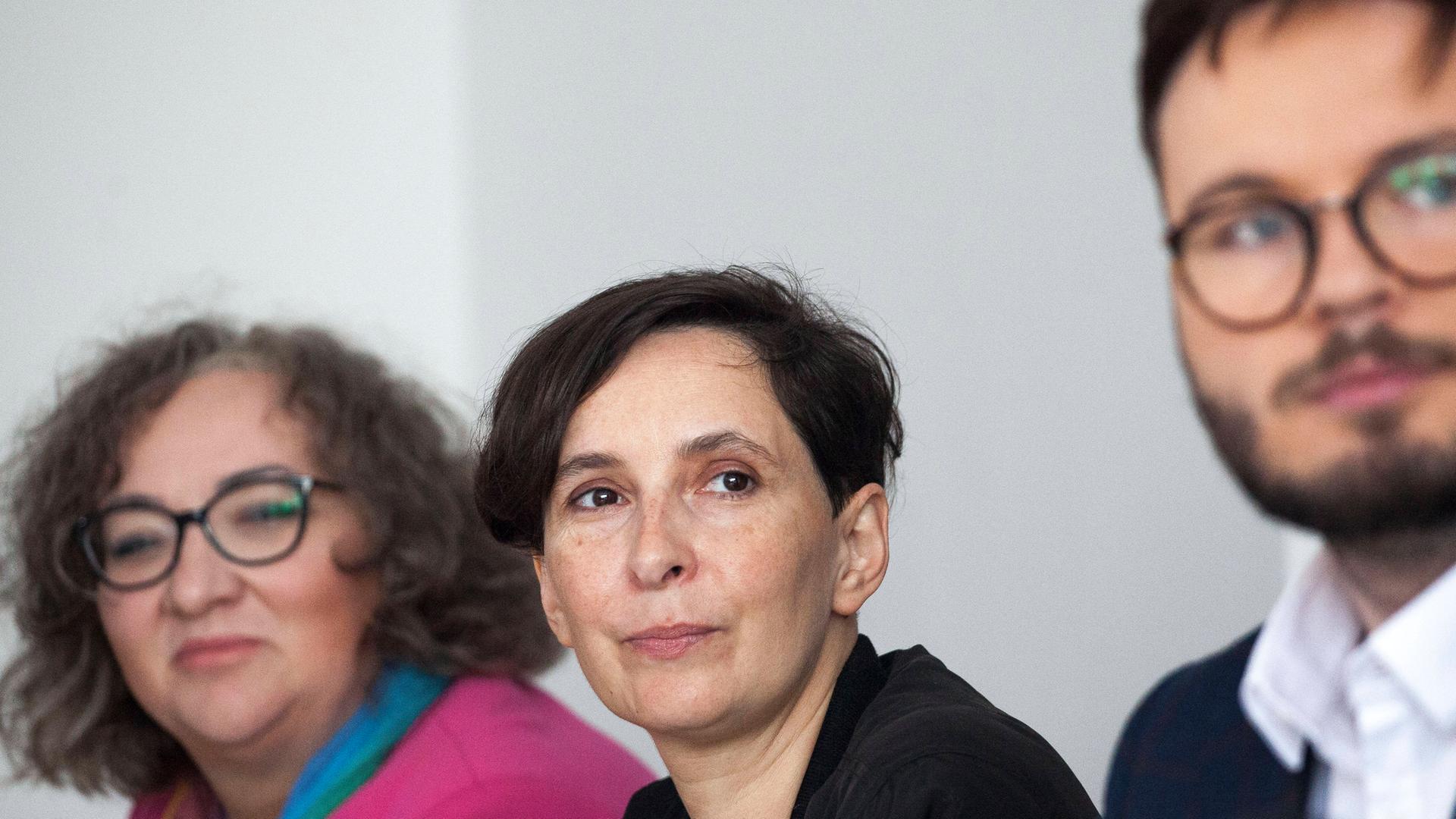 Frau sitzt zwischen zwei Personen u d schaut in die Kamera