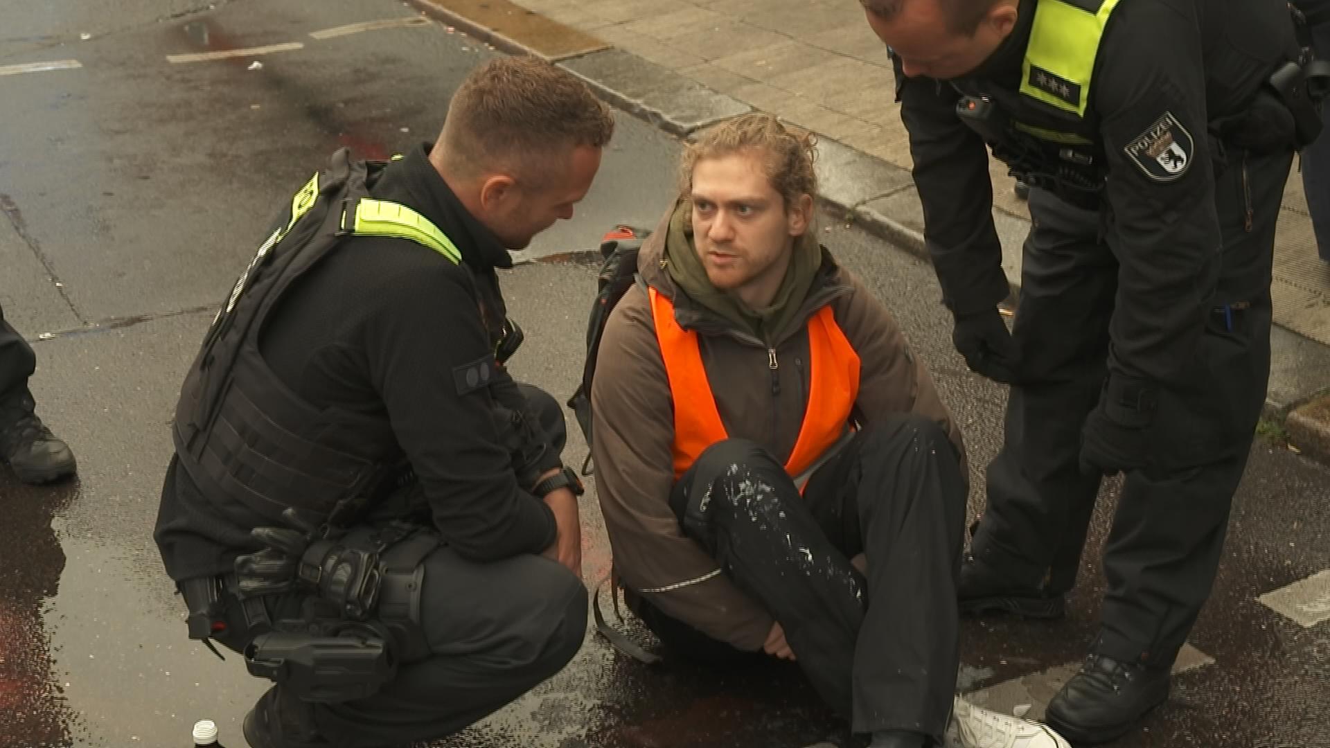 Klima-Aktivist sitzt auf der Straße und diskutiert mit Polizisten