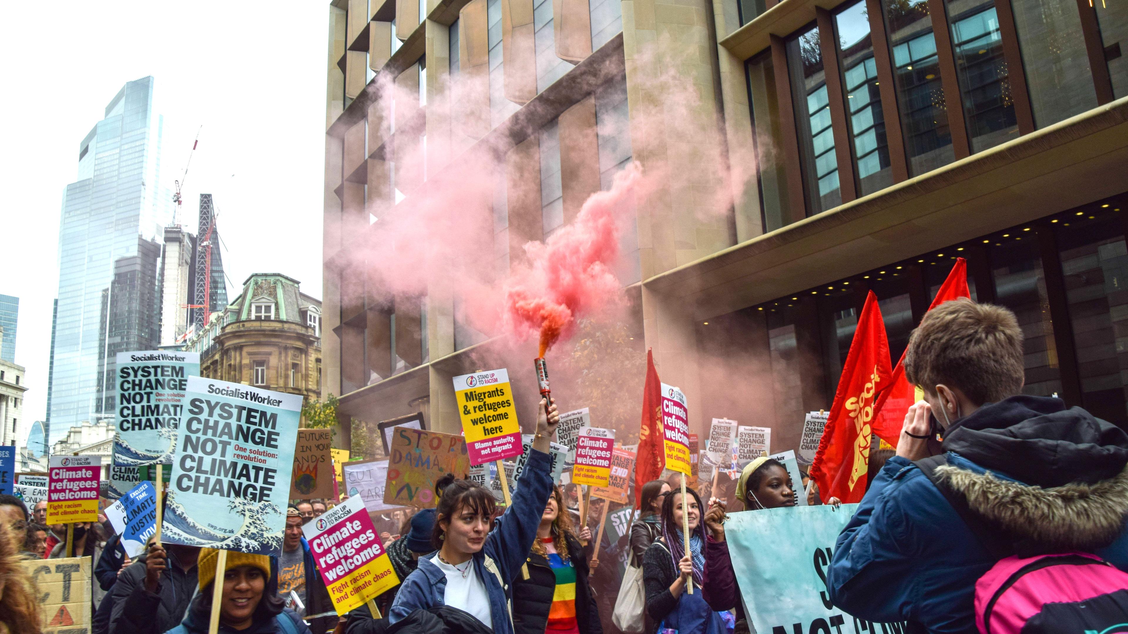 Auf einer Straße in London laufen junge Menschen bei einer Demonstration für das Klima mit Schildern und Pyrotechnik.