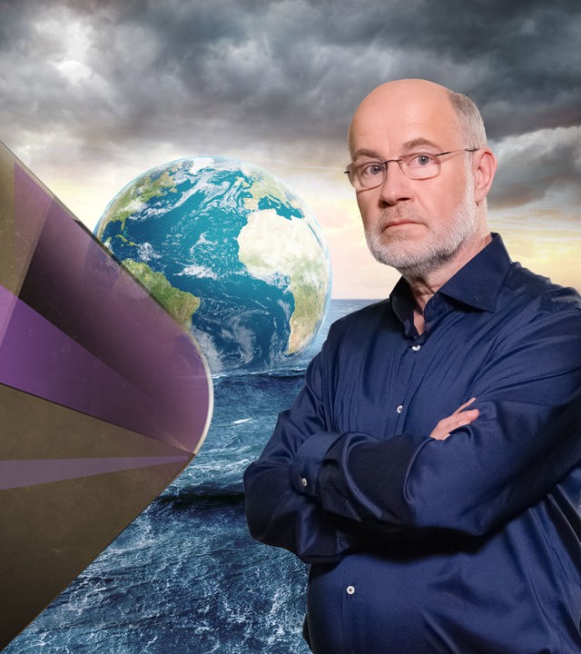 Professor Harald Lesch steht vor Meer mit schwimmender Erdkugel