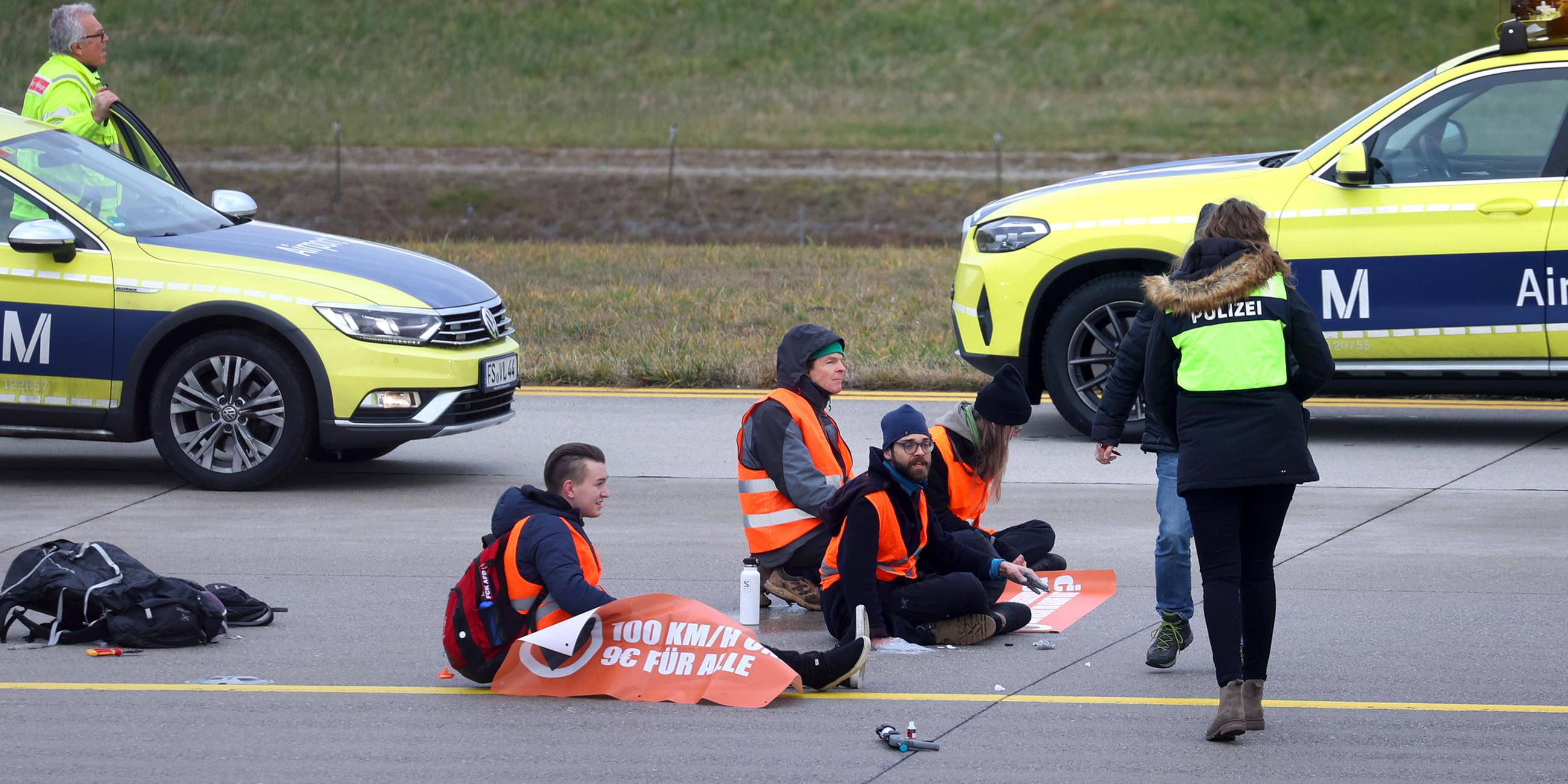 Vier Klimaaktivisten sitzen mit angeklebten Händen auf dem Zubringer einer Start-und Landebahn am Airport Franz-Josef-Strauß.
