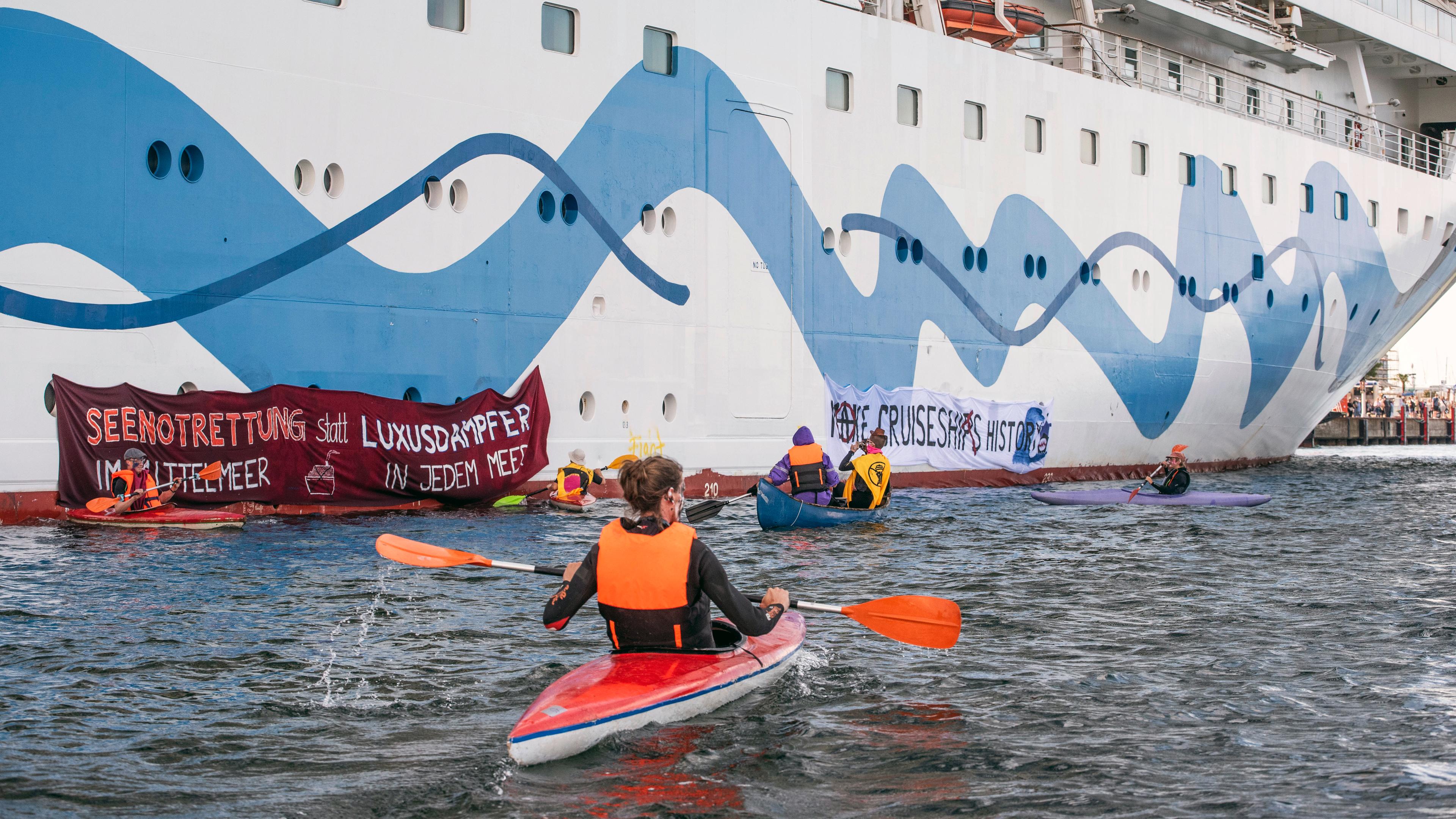 Klimaaktivisten mit Warnwesten paddeln in Kayaks um ein Kreuzfahrtschiff 
