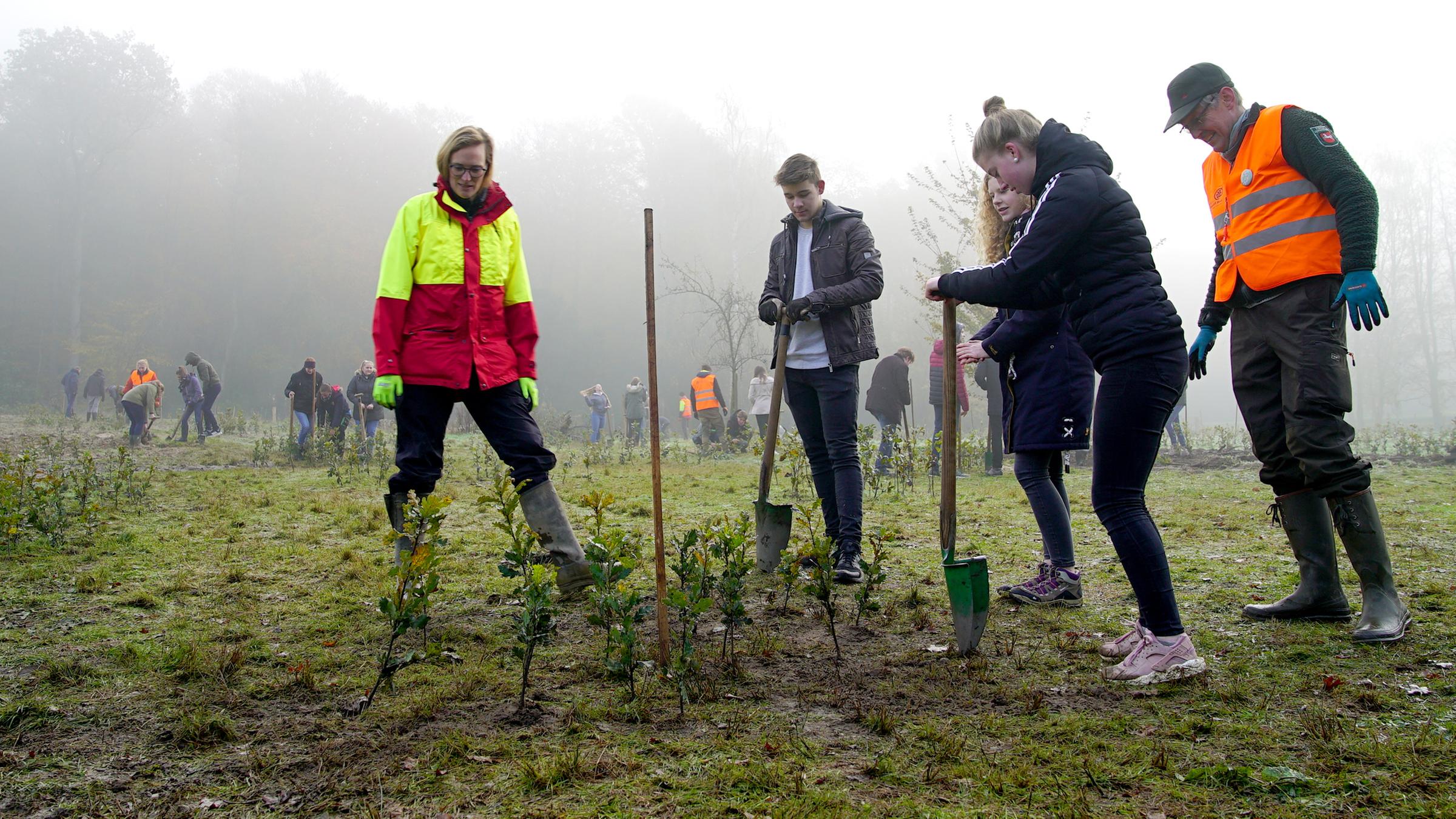 Elisabeth Hüsing steht neben drei jungen Menschen, die Bäume pflanzen.