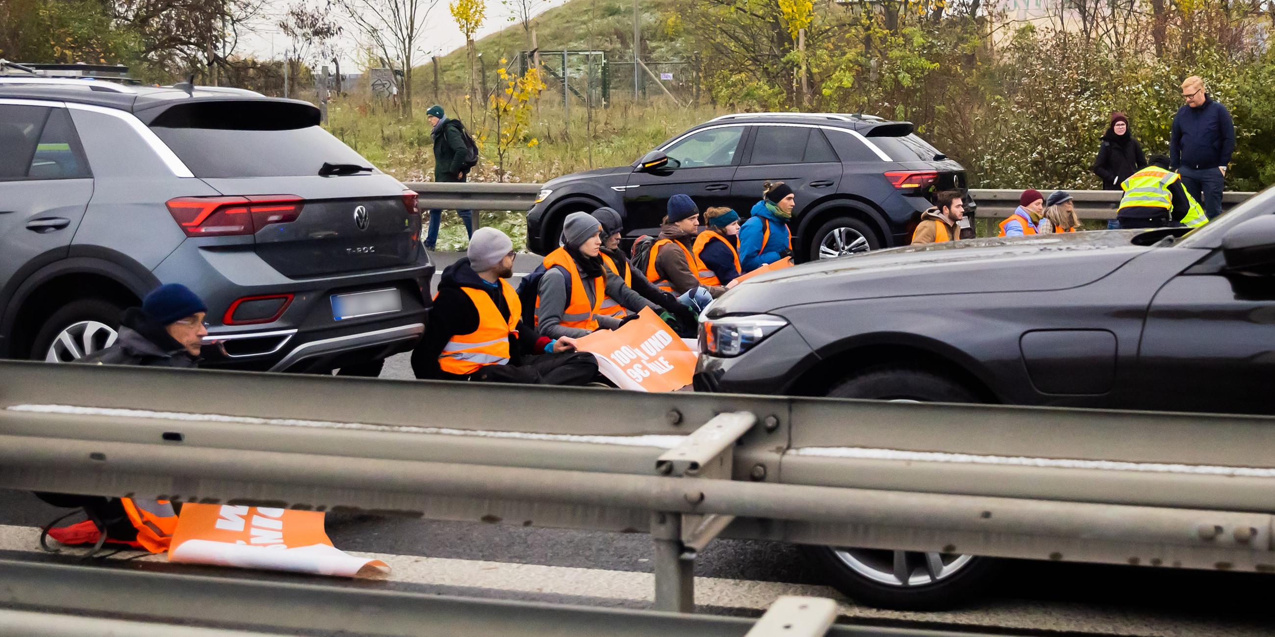 Das Bild zeigt Klimaaktivisten der selbsternannten "Letzten Generation", die auf der A113 kurz vor der Ausfahrt zum Flughafen Berlin Brandenburg (BER) den Verkehr blockieren.