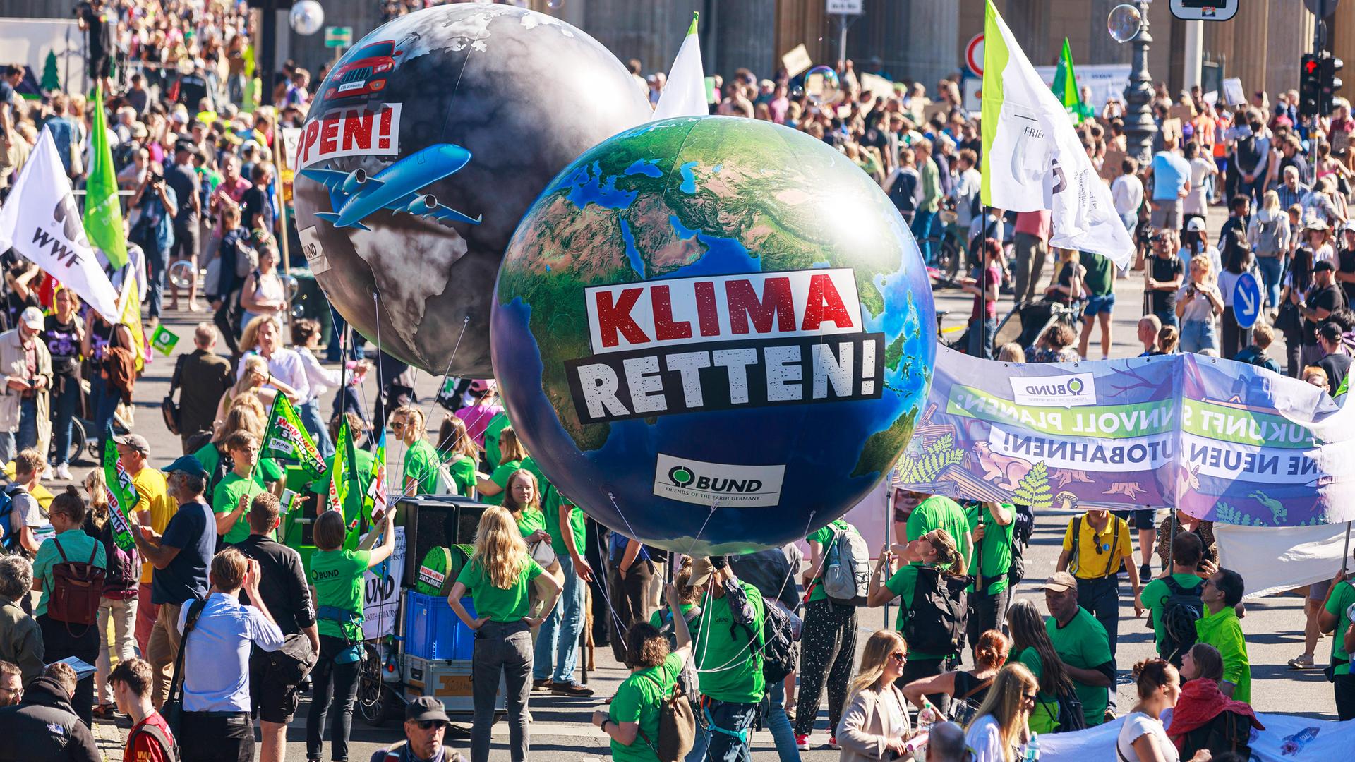 Auf einer Demonstration für die Rettung des Klimas wuseln viele Menschen mit Flaggen, Bannern und zwei riesigen Luftballons in Form der Erde durcheinander.