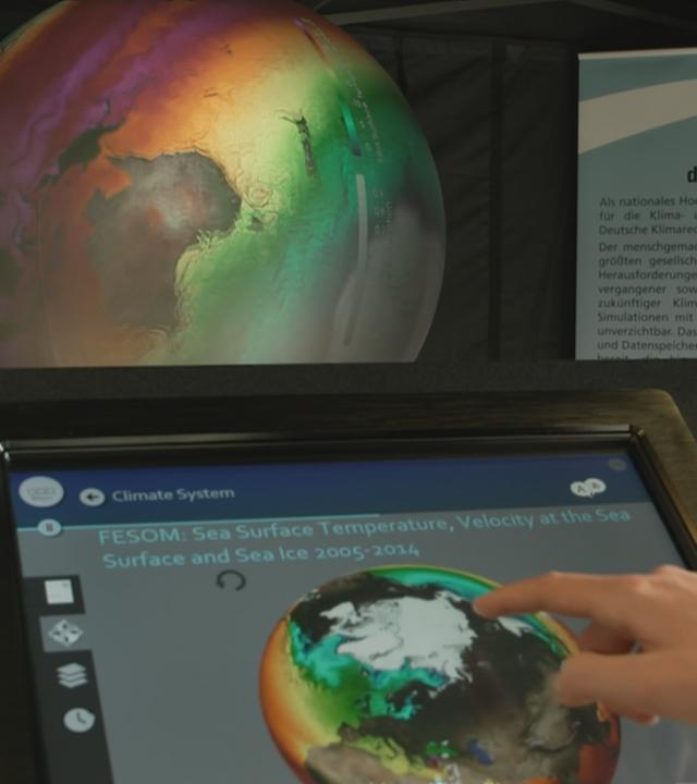 Hand zeigt auf Bildschirm mit Globus im Hintergrund