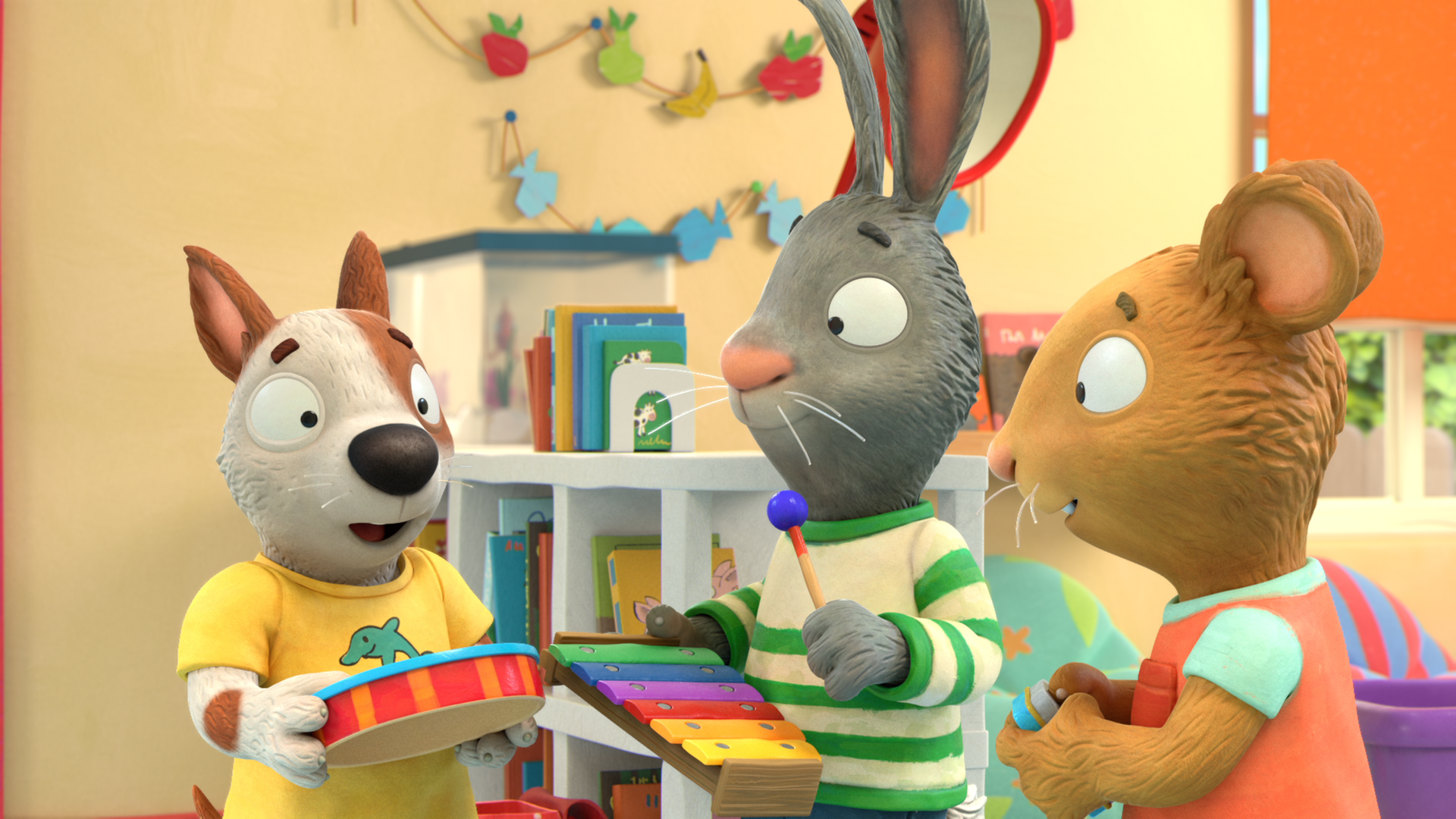 Zac steht links mit seiner orange-rot-gestreiften Trommel, in der Mitte Pip mit einem bunten Xylophon und rechts Posy mit einer Rassel. Die drei unterhalten sich. Im Hintergrund des Kinderzimmers ist ein Regal mit Büchern zu sehen und zwei Girlanden an der Wand.