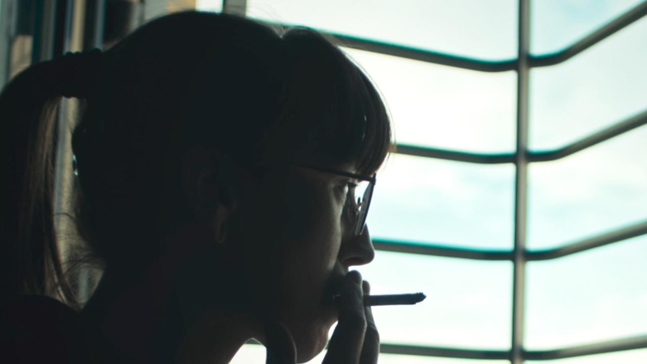 Eine junge Gefängnisinsassin sitzt rauchend vorm vergitterten Fenster.