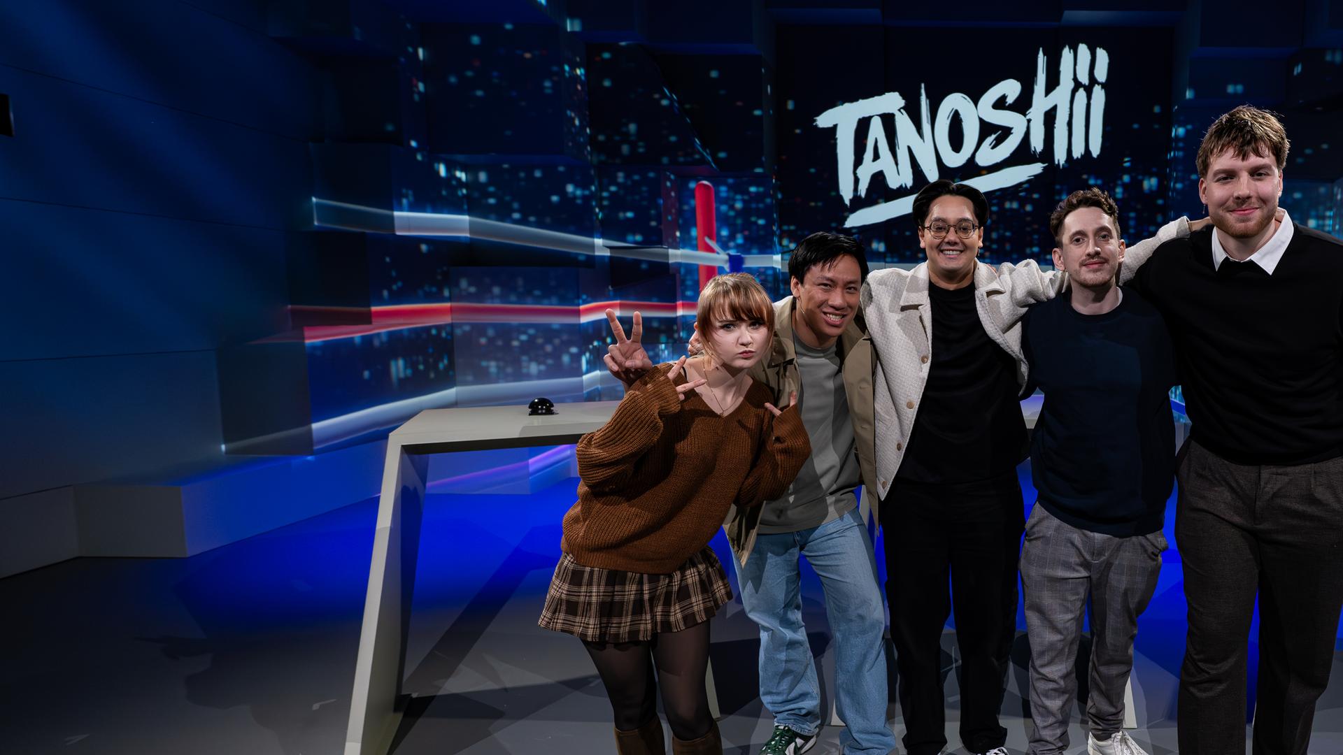 v. l. n. r. Kaddicosplay, Viet, Moderator Raafey, JustNero und Anigents. Alle fünf stehen Arm in Arm vor der Tanoshii-Studiokulisse und lächeln in die Kamera. Mittig über ihnen ist das Tanoshii-Logo zu sehen.