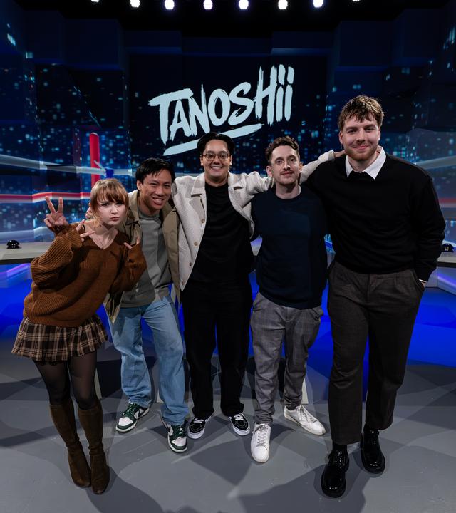 v. l. n. r. Kaddicosplay, Viet, Moderator Raafey, JustNero und Anigents. Alle fünf stehen Arm in Arm vor der Tanoshii-Studiokulisse und lächeln in die Kamera. Mittig über ihnen ist das Tanoshii-Logo zu sehen.