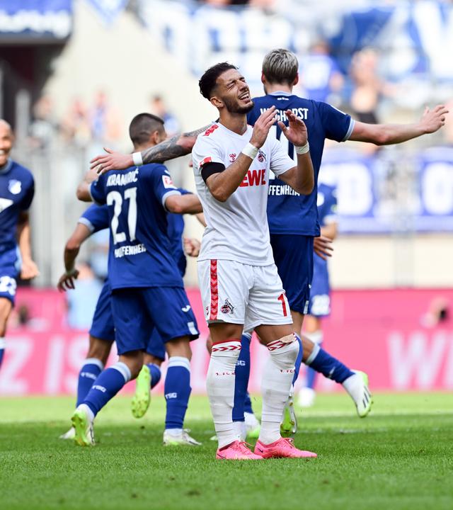 Kölns Leart Paqarada ist enttäuscht, während Hoffenheims Spieler das Tor zum 0:2 im RheinEnergieStadion am 16.09.2023 bejubeln.