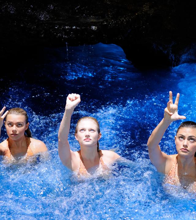 Rikki, Bella und Cleo sind im sprudelnden Mondsee. Alle drei strecken ihren jeweils rechten Arm nach oben aus und machen eine magische Bewegung. Dabei blicken sie angestrengt nach oben.