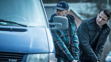 Oskar Bergman (Måns Nathanaelson) und ein Kollege nehmen Deckung hinter einem Auto
