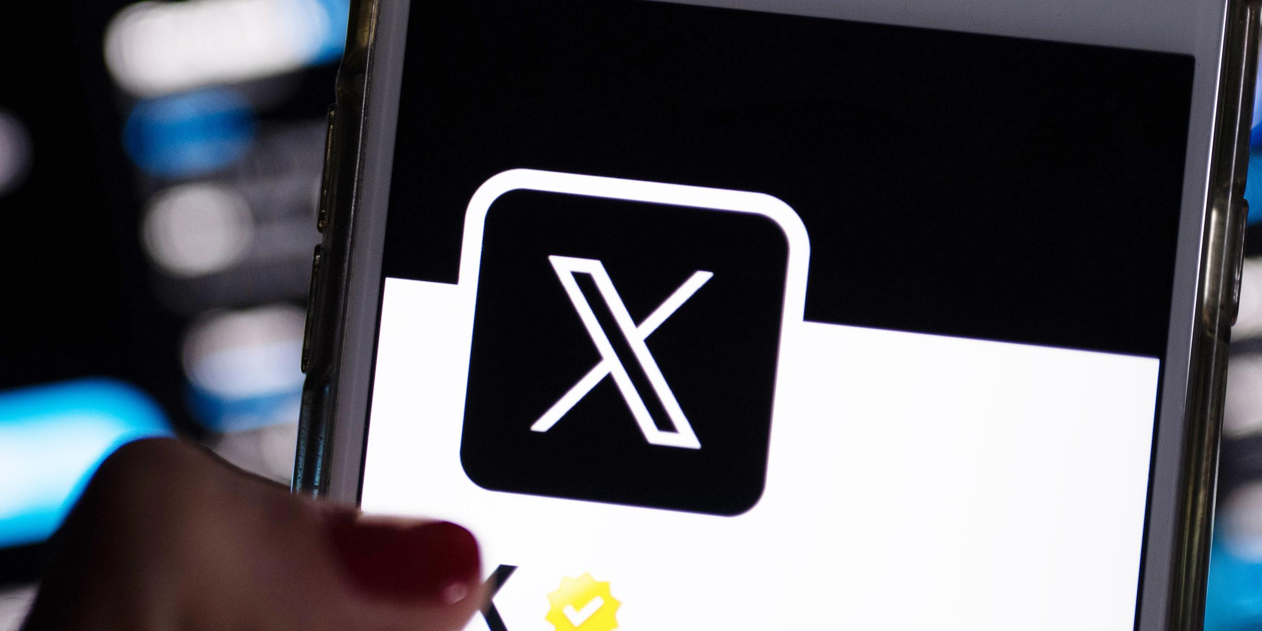 Auf dem offiziellen Profil der Plattform X auf dem Bildschirm eines Smartphones ist der weiße Buchstabe X auf schwarzem Hintergrund zu sehen.