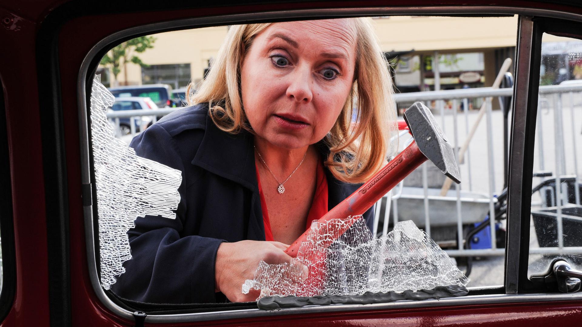 "Dr. Klein - Konsequenzen": Dr. Valerie Klein (ChrisTine Urspruch) steht vor der Fahrertür ihres Wagens mit einem Hammer in der Hand und betrachtet die eingeschlagene Autofensterscheibe.