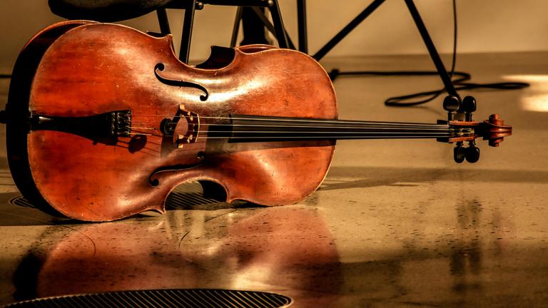 Ein Cello liegt waagerecht neben einem Stuhl auf dem Boden