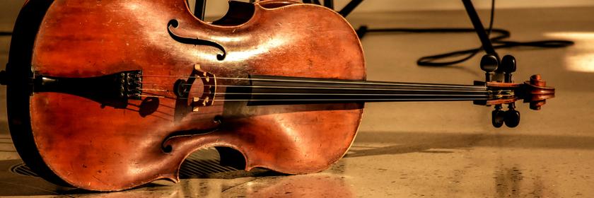 Ein Cello liegt waagerecht neben einem Stuhl auf dem Boden