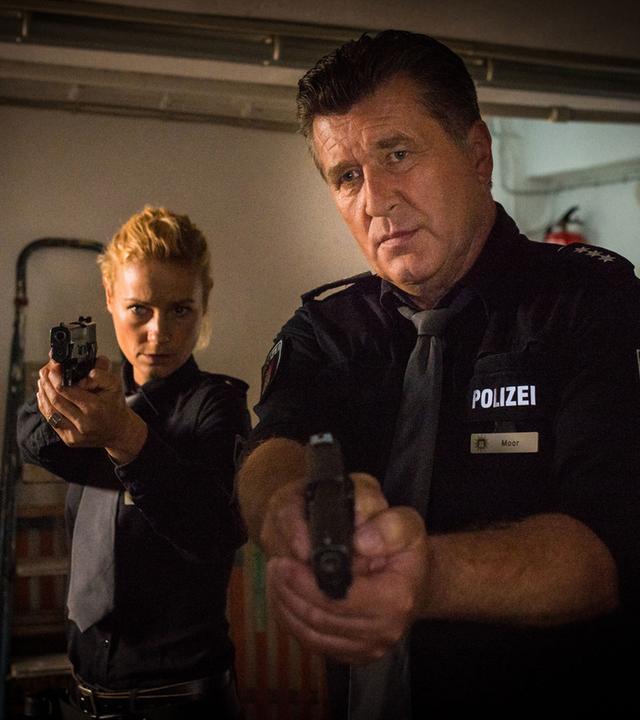 "Notruf Hafenkante - Kopfgeld": Die Polizisten Franzi Jung (Rhea Harder-Vennewald) und Hans Moor (Bruno F. Apitz) gehen nebeneinander mit gezogenen Waffen durch einen Kellerraum.