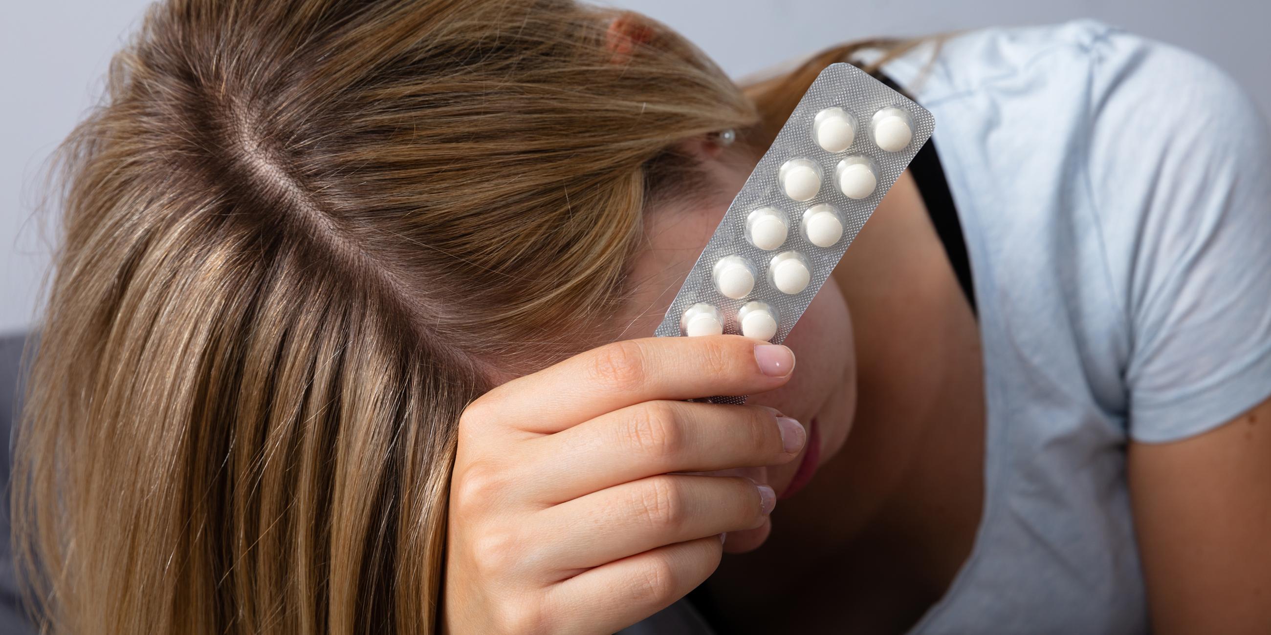 Frau mit Kopfschmerzen hält Tabletten in der Hand