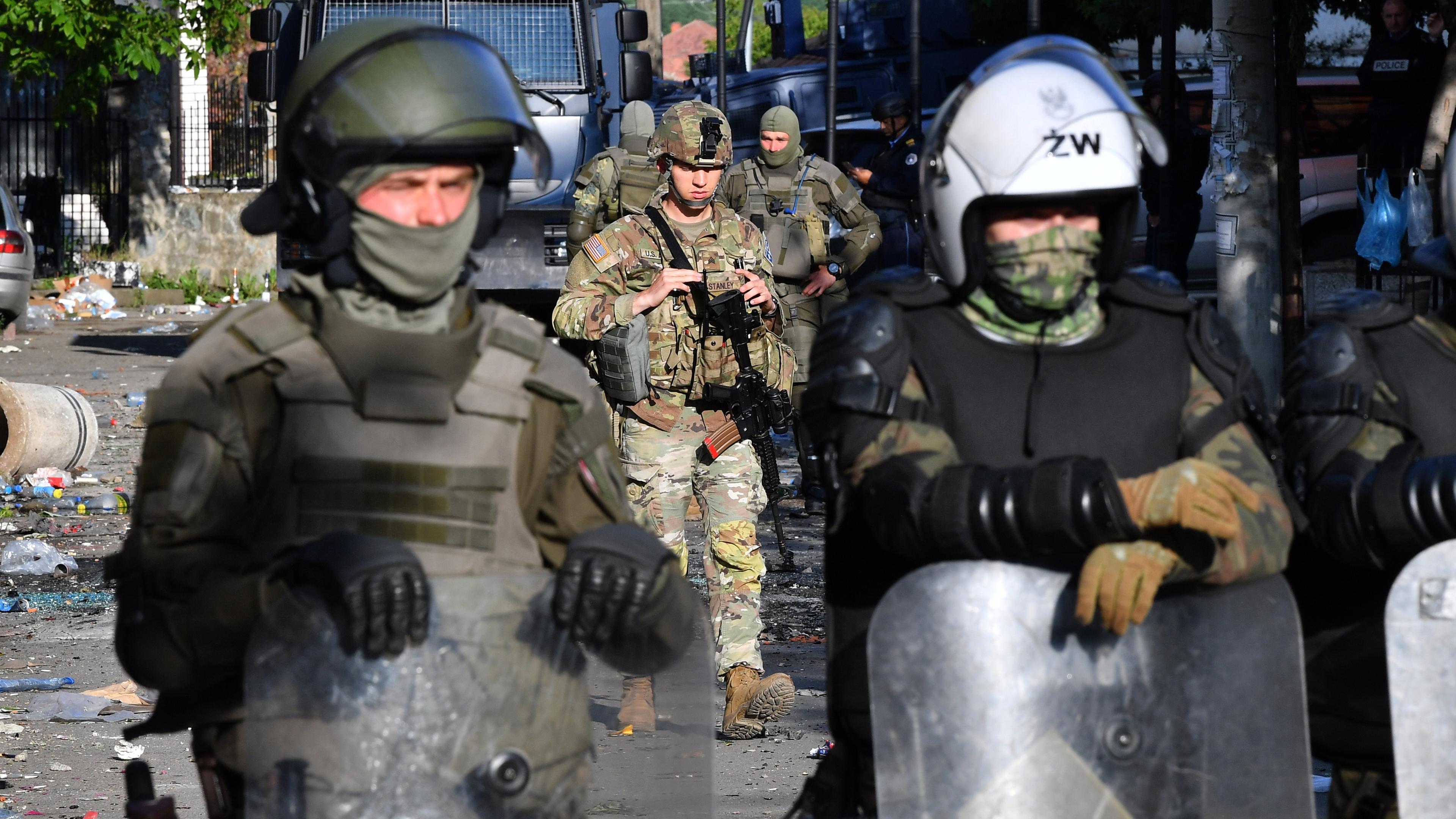 Zu sehen sind Soldaten einer NATO-Friedensmission mit Schutzschildern und schwerer Ausrüstung.