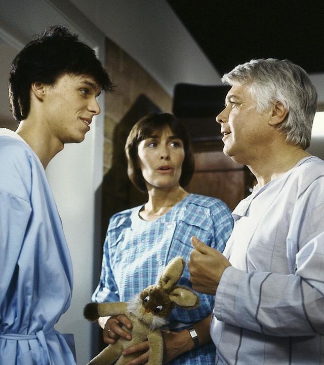 Werner ist im Gespräch mit einem Mann in OP-Klamotten und einer Frau, die einen Stoffhasen in der Hand hält.