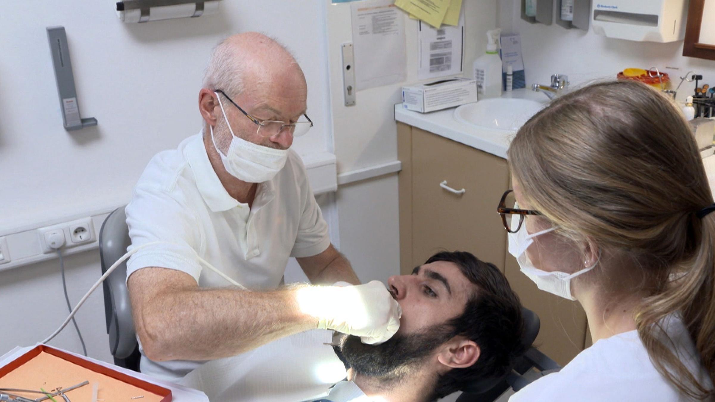 "Krank ohne Kasse - Wenn das Gesundheitssystem versagt": Ein Zahnarzt und eine Helferin behandeln einen jungen Mann, der zwischen den beiden auf dem Behandlungsstuhl liegt.