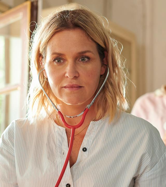 "Lena Lorenz - Krank vor Sorge": Auf einer Untersuchungsliege liegt Tati Meisinger (Anouk Elias) und blickt zur Decke. Lena Lorenz (Judith Hoersch) hat neben ihr Platz genommen und schaut sie besorgt an. Praktikantin Celine (Paulina Rümmelein) steht neben dem Kopfteil der Liege und beobachtet interessiert das Geschehen.