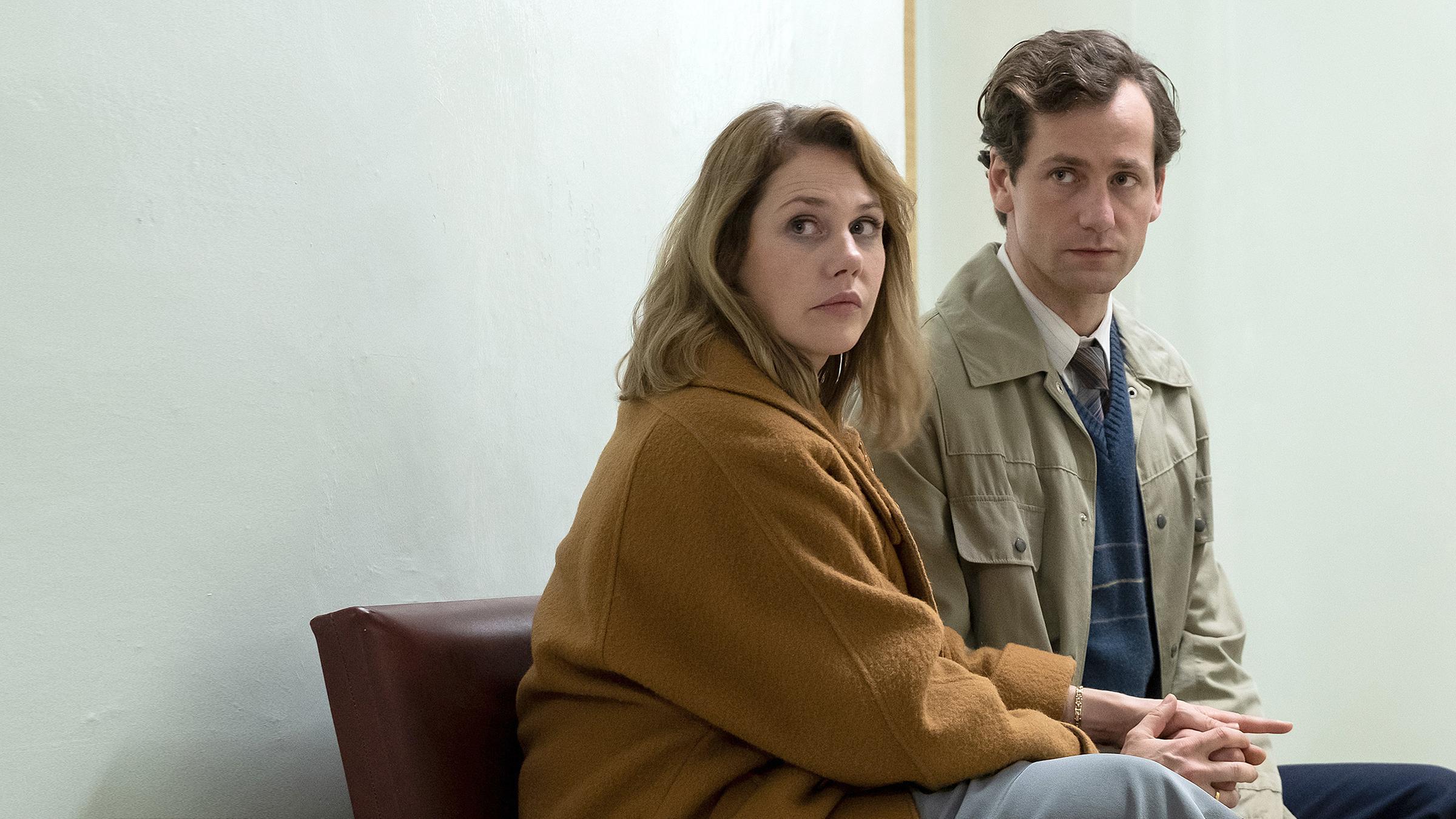 Marie Glaser (Felicitas Woll) und Armin Glaser (Florian Stetter) sitzen auf einer gepolsterten Sitzbank im Flur des Krankenhauses und schauen erwartungsvoll in die gleiche Richtung. Marie umklammert Armins Hände.