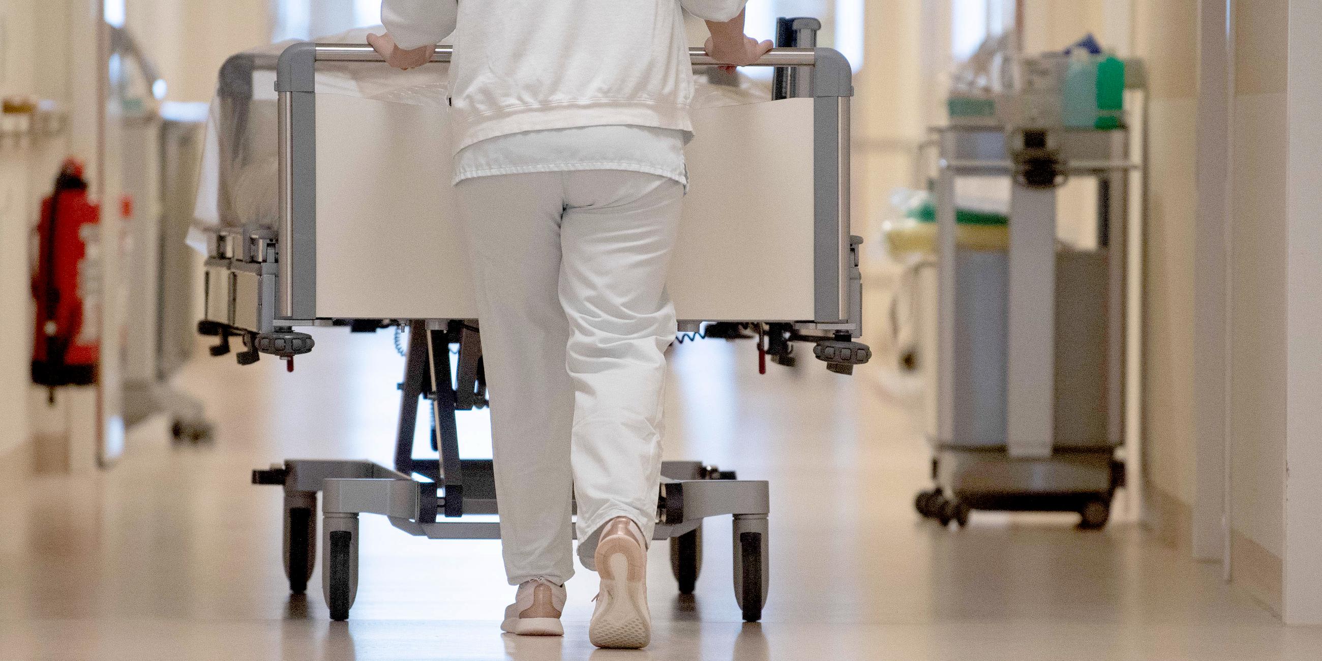 Eine Krankenpflegerin schiebt ein Krankenbett durch einen Krankenhausflur