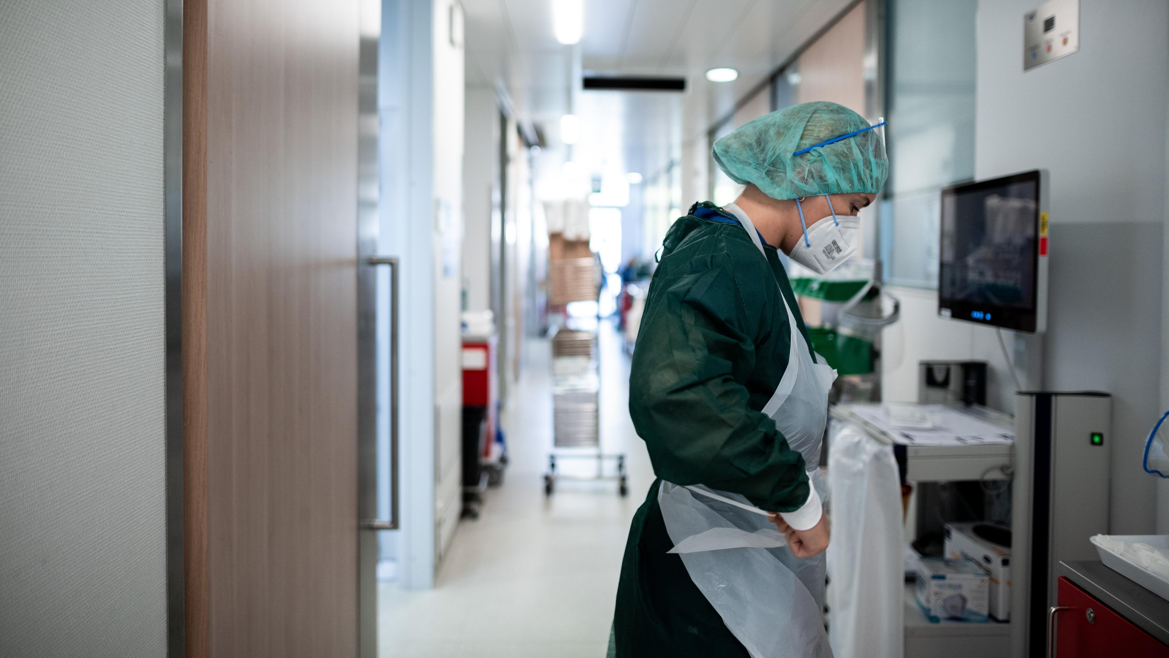 Nordrhein-Westfalen, Essen: Eine Mitarbeiterin der Pflege steht auf dem Gang der Corona-Intensivstation des Universitätsklinikums Essen und zieht Schutzkleidung an.