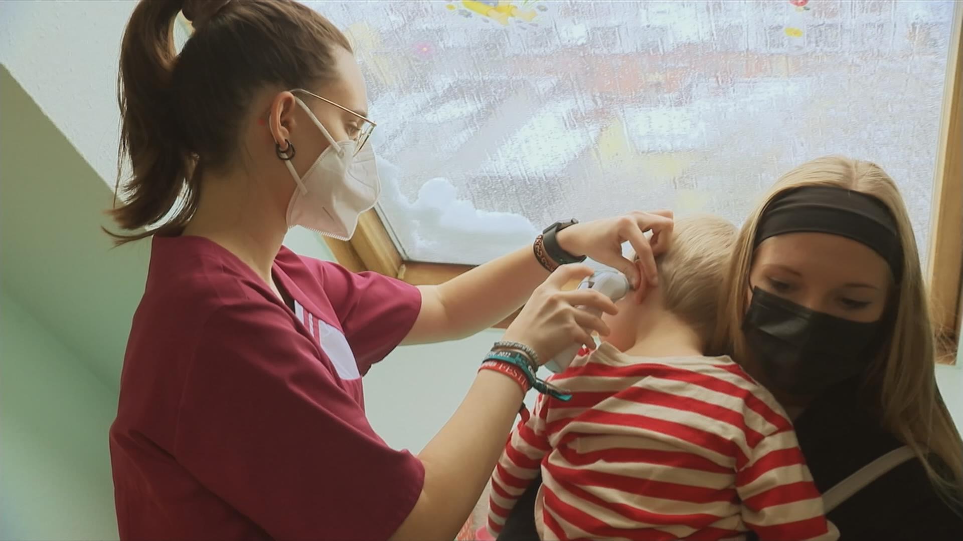 Krankenschwester untersucht Kleinkind auf dem Arm seiner Mutter.