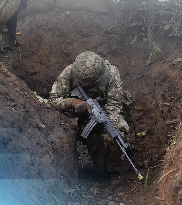 Ein ukrainischer Soldat, bewaffnet und in Uniform geduckt in einem Graben.