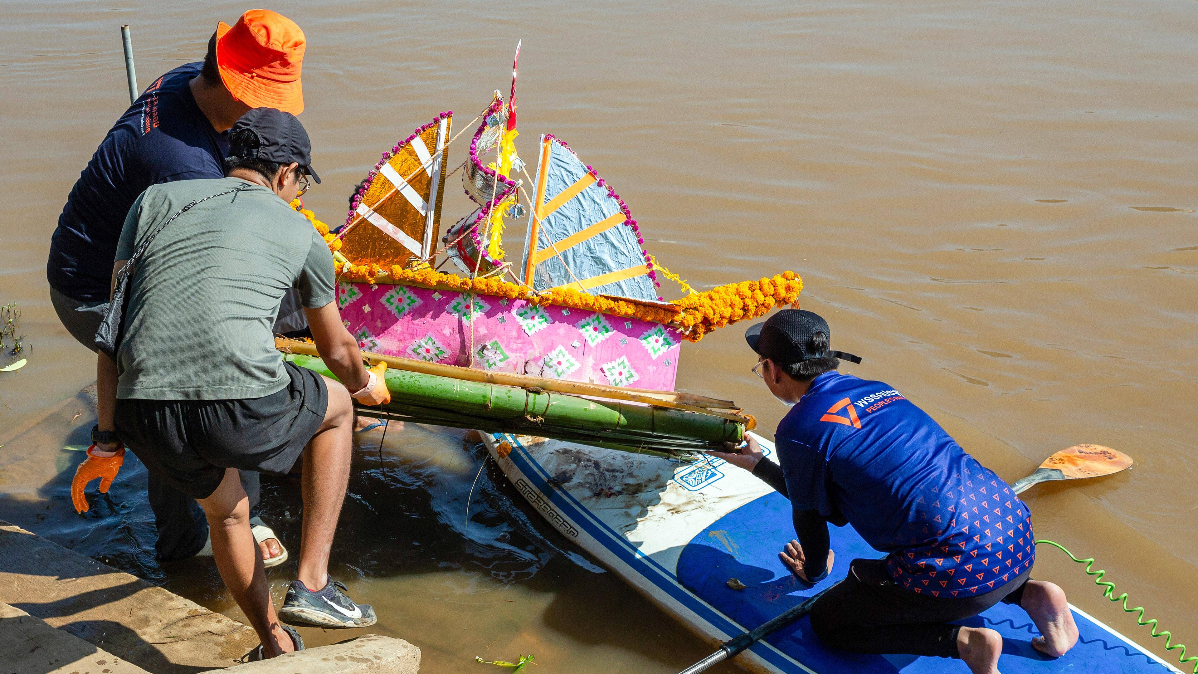Bunt dekorierte Stofflaterne auf Bambusfloß, die von Helfern aus dem Wasser geholt wird.