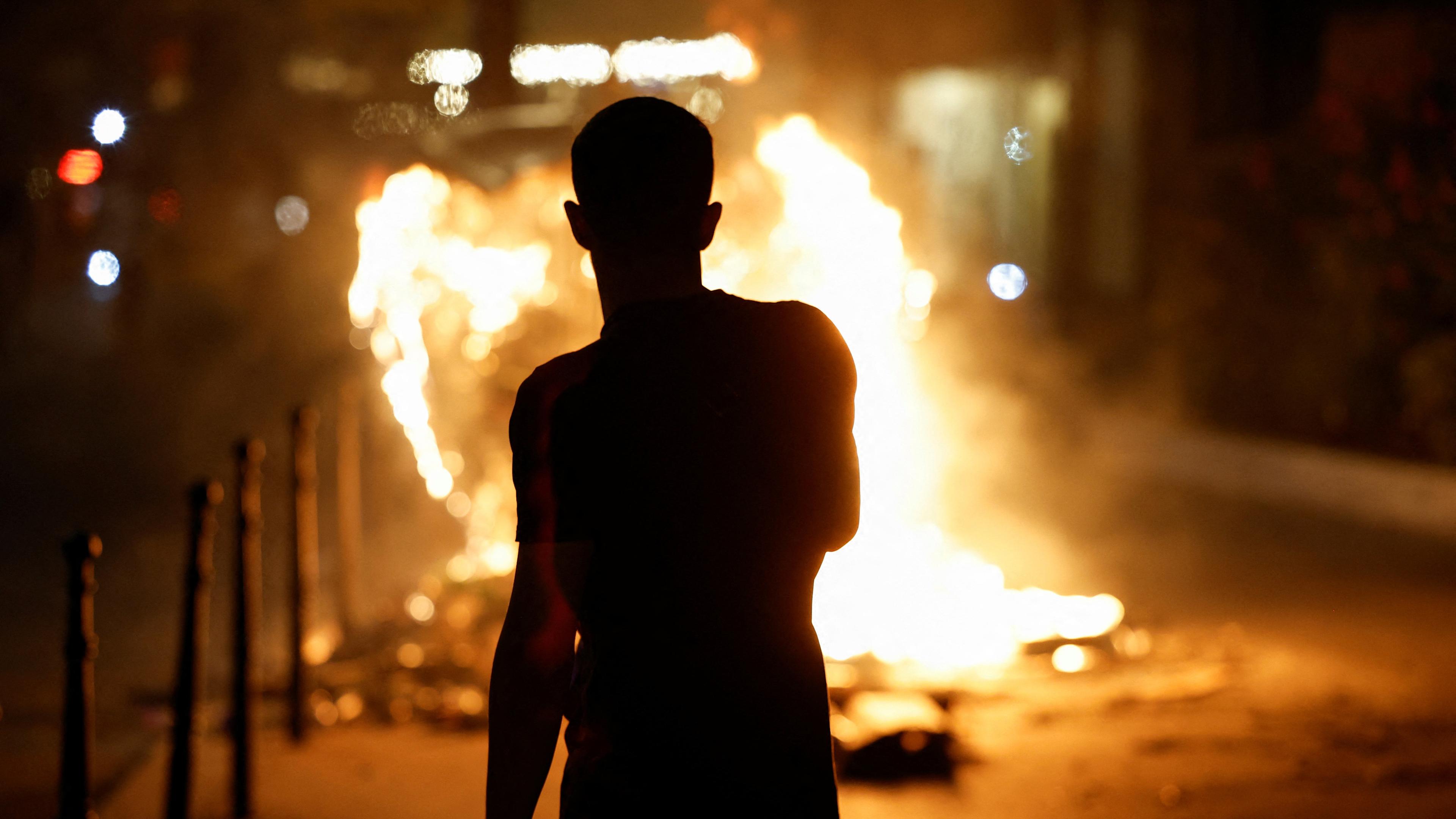 Eine Person steht in der Nähe eines brennenden Containers, während Menschen nach dem Tod von Nahel, einem 17-jährigen Teenager, der von einem französischen Polizisten in Nanterre bei einer Verkehrskontrolle getötet wurde, und gegen Polizeigewalt in Paris, Frankreich, am 30. 06. 2023 protestieren . 