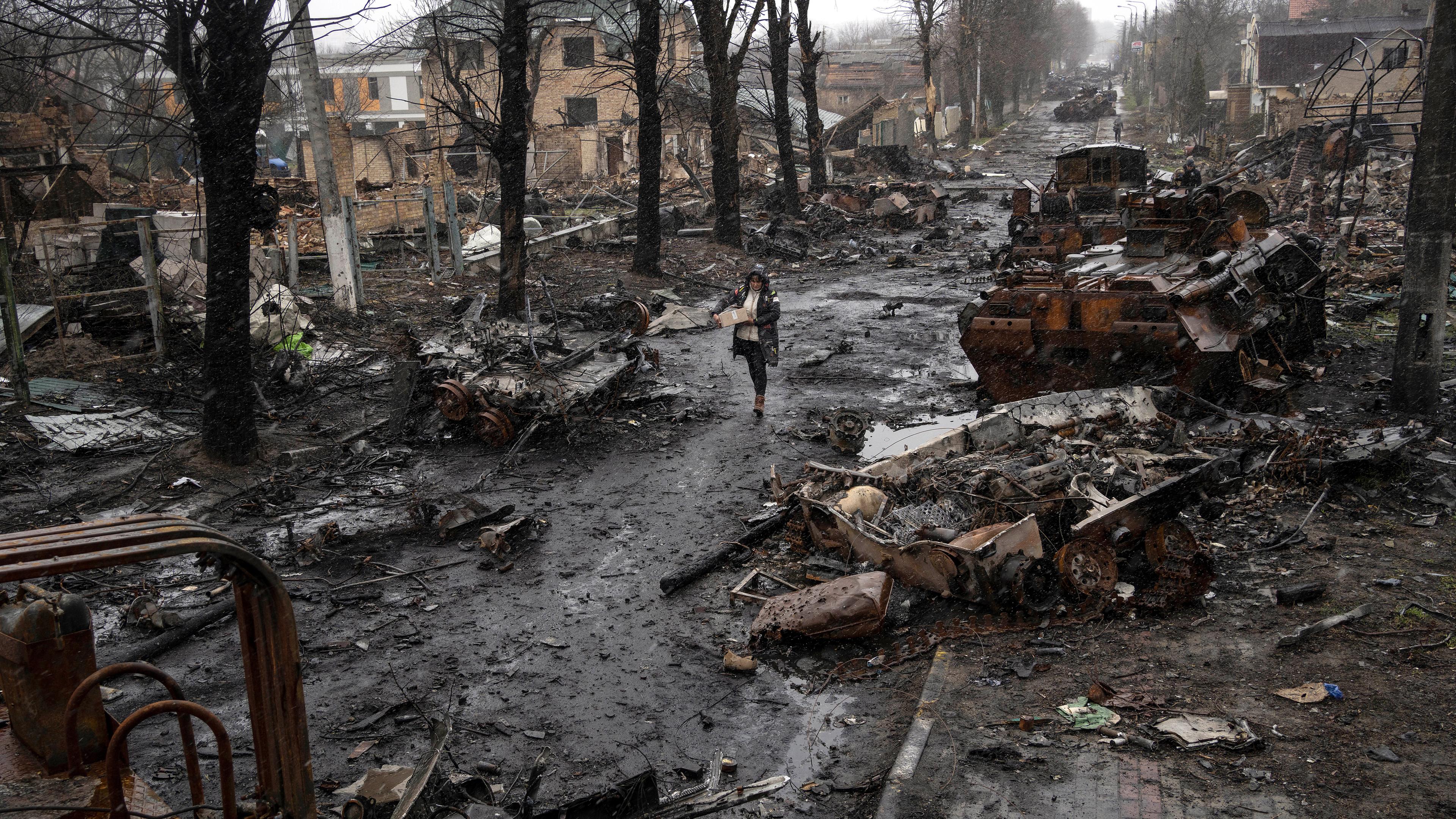 Eine Frau geht auf einer Straße, die übersät ist mit zerstörten russischen Militärfahrzeugen, aufgenommen am 03.04.2022