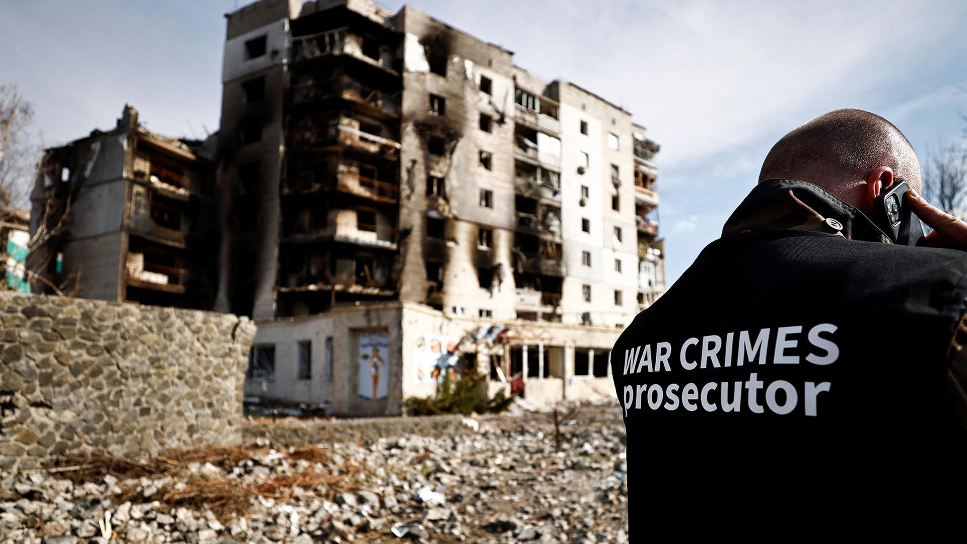 Kriegsverbreche-Ermittler in der Ukraine vor einem zerstörten Gebäude.