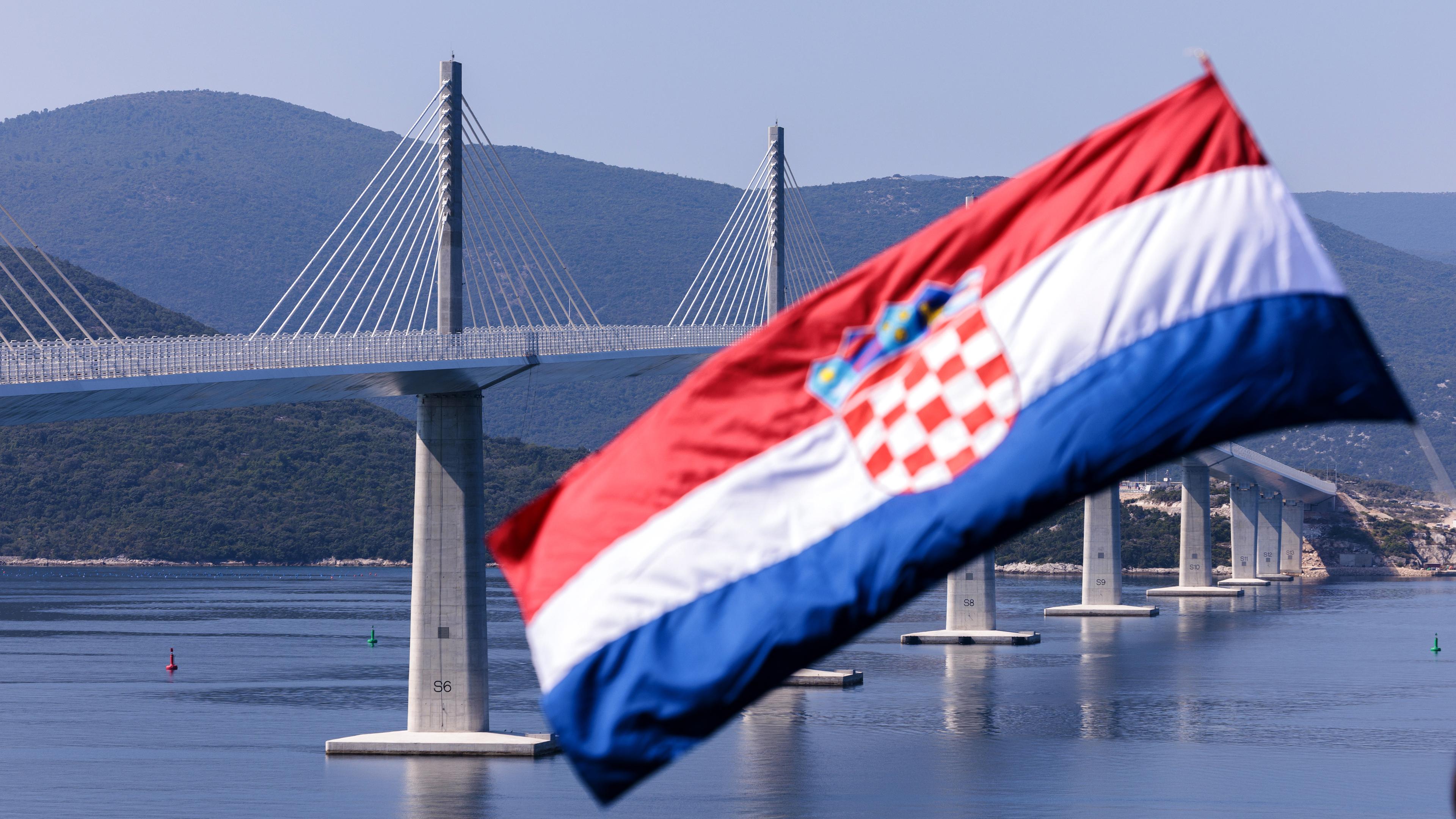 Kroatische Flagge weht im Wind, im Hintergrund ist die Peljesac-Brücke