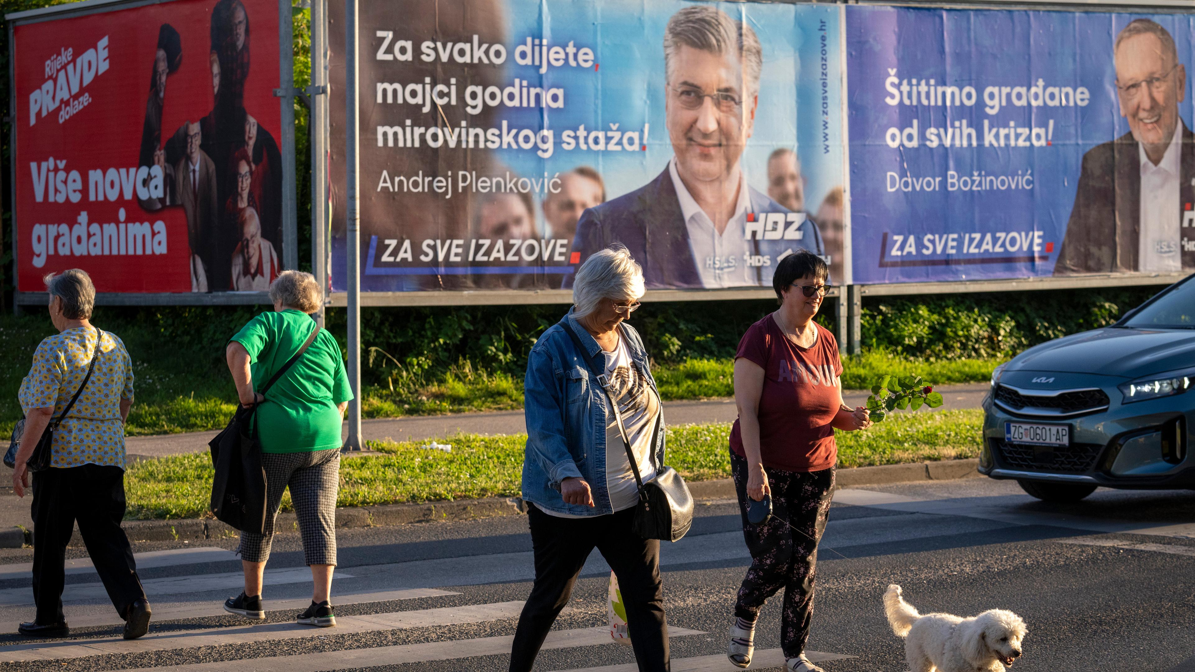 Fußgänger überqueren eine Straße vor Wahlplakaten in Zagreb, Kroatien, am Sonntag, 14.04.2024