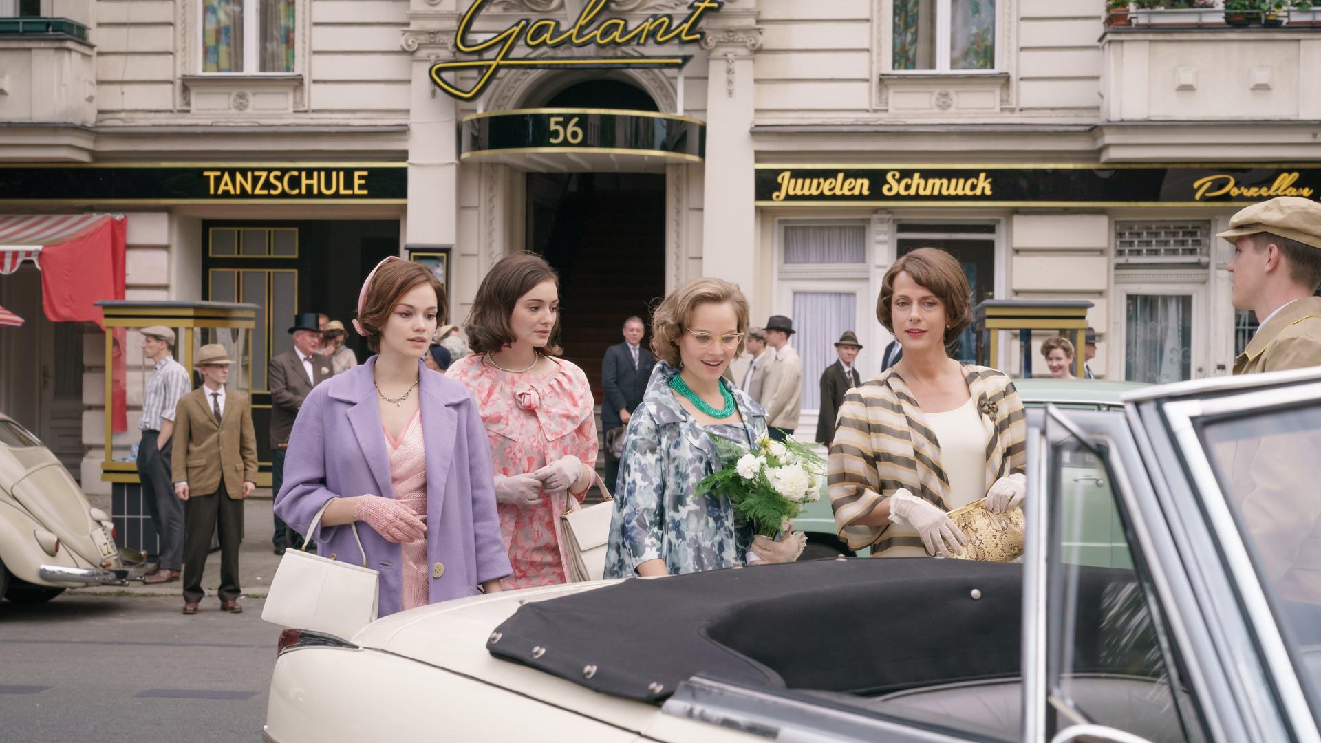Eva Fassbender geb. Schöllack (Emilia Schüle, l.), Helga von Boost (Maria Ehrich, 2.v.l.), Monika Schöllack (Sonja Gerhardt, 3.v.l.) und Caterina Schöllack (Claudia Michelsen, 4.v.l.) auf dem Weg zum Standesamt. "Ku'damm 59"; Teil 3: Eva Fassbender geb. Schöllack (Emilia Schüle), Caterina Schöllack (Claudia Michelsen), Helga von Boost (Maria Ehrich )und Monika Schöllack (Sonja Gerhardt) gehen gemeinsam die Straße vor der Tanzschule entlang zu einem Auto