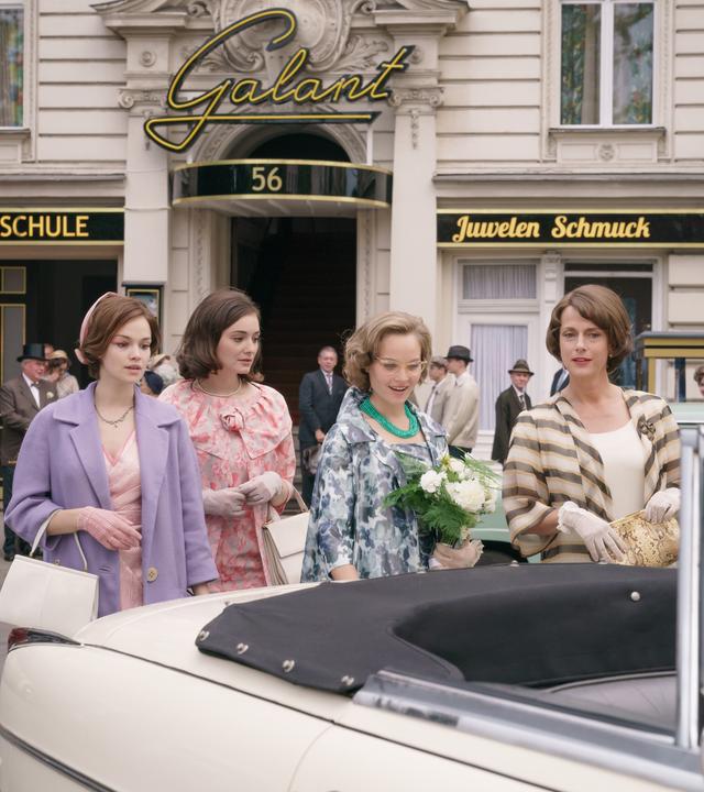 Eva Fassbender geb. Schöllack (Emilia Schüle, l.), Helga von Boost (Maria Ehrich, 2.v.l.), Monika Schöllack (Sonja Gerhardt, 3.v.l.) und Caterina Schöllack (Claudia Michelsen, 4.v.l.) auf dem Weg zum Standesamt. "Ku'damm 59"; Teil 3: Eva Fassbender geb. Schöllack (Emilia Schüle), Caterina Schöllack (Claudia Michelsen), Helga von Boost (Maria Ehrich )und Monika Schöllack (Sonja Gerhardt) gehen gemeinsam die Straße vor der Tanzschule entlang zu einem Auto