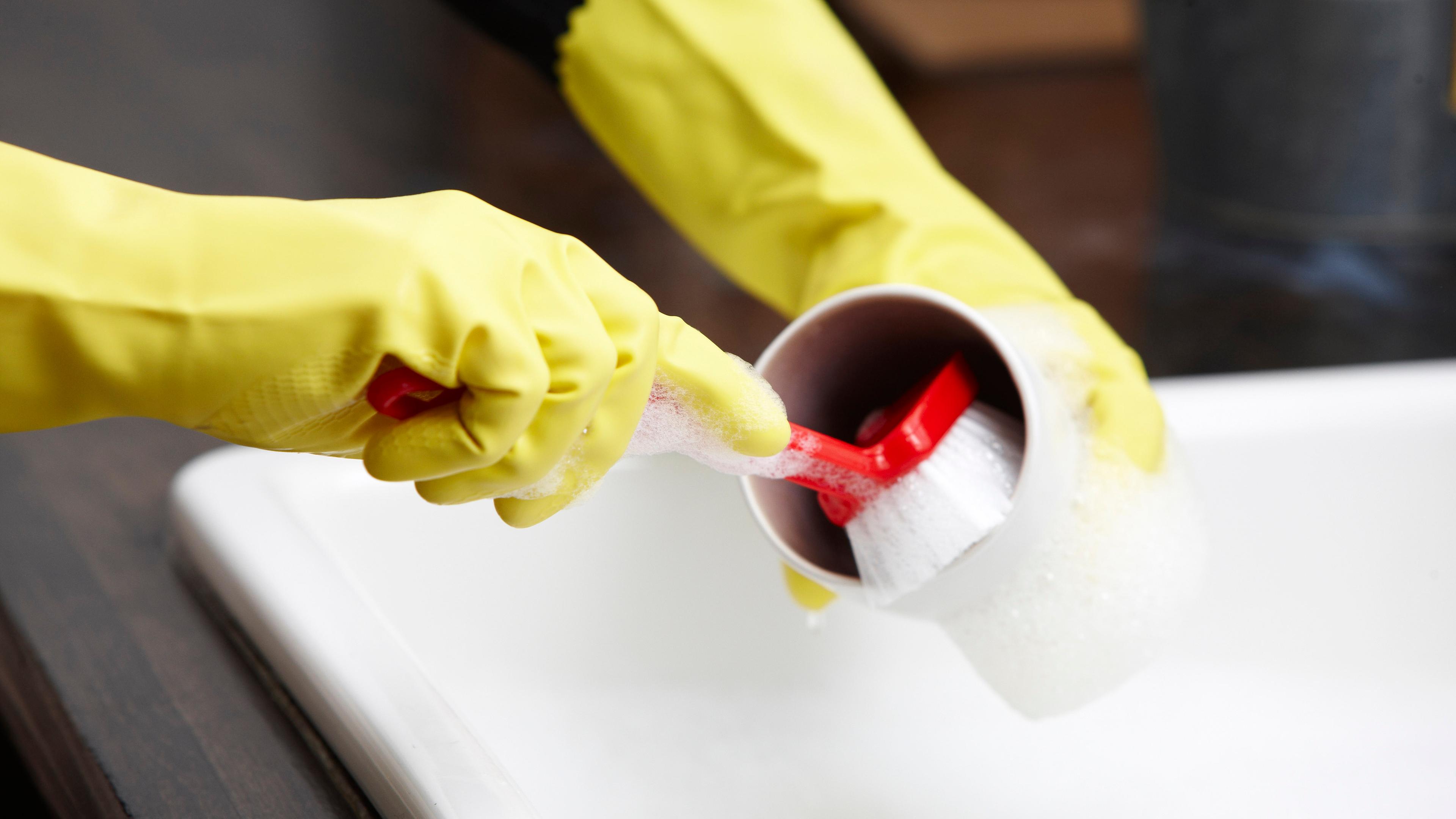 Person beim Abwasch mit gelben Handschuhen und Spülbürste