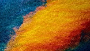 Abstraktes Bild: Körnige Farbflächen verlaufen von kühlem Blau zu warmen Gelb- und Rottönen und bilden eine diffuse, wolkenähnliche Struktur. Das Bild erzeugt den Eindruck eines abstrakten Himmels.