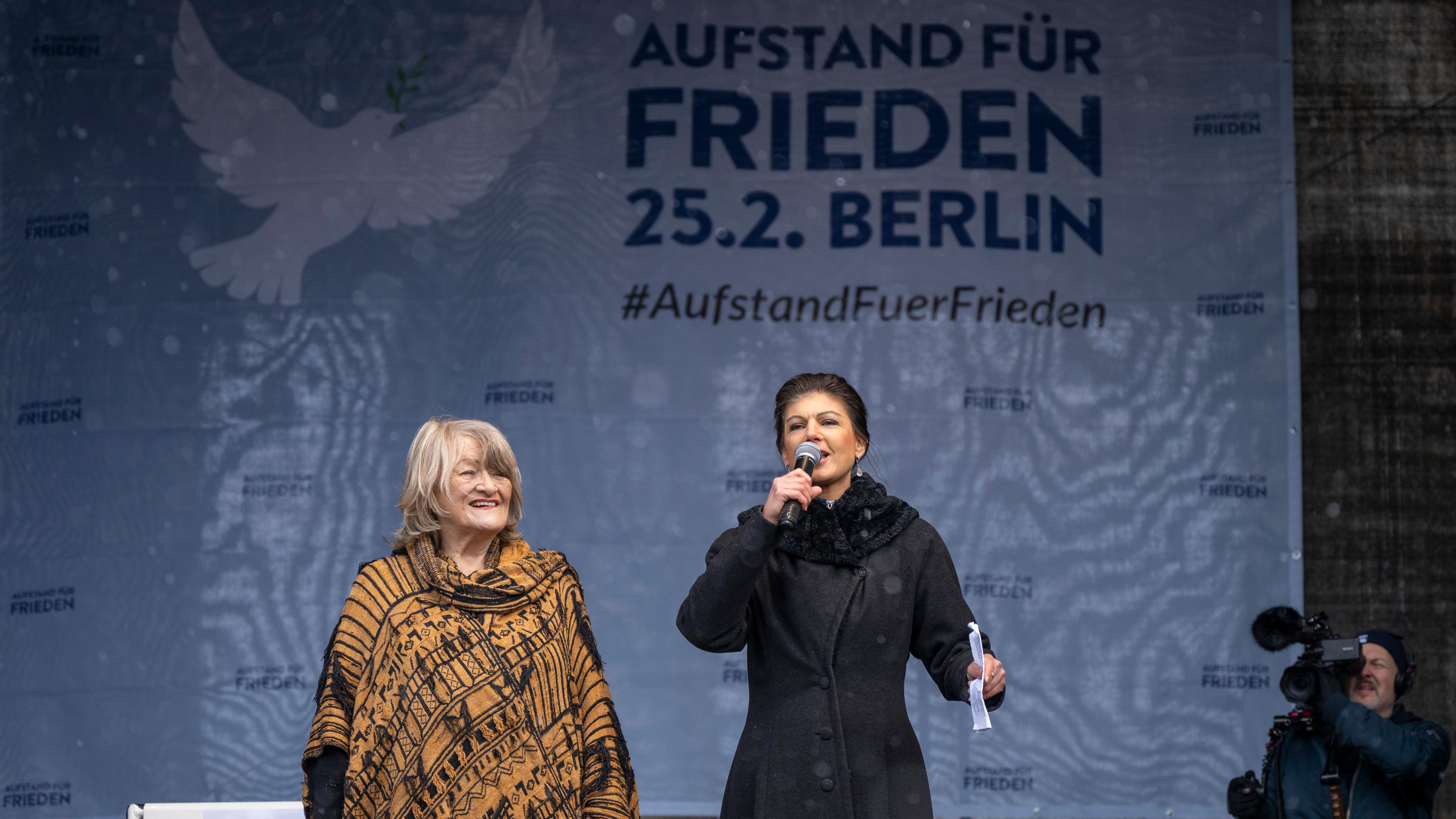 Women's rights activist Alice Schwarzer and left-wing politician Sahra Wagenknecht stand on a stage and speak into a microphone.