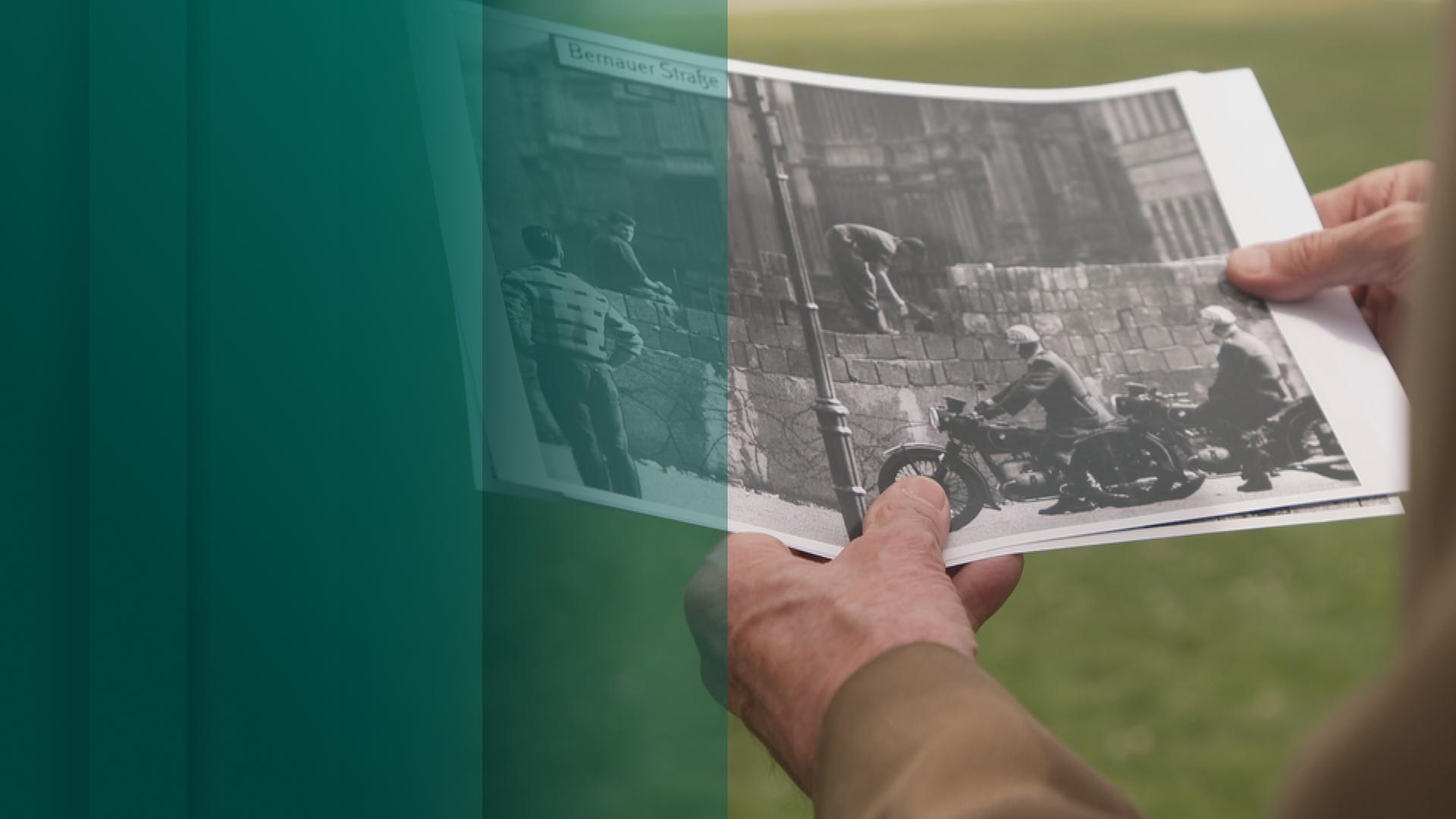 Mann hält Bild vom Bau der Berliner Mauer in der Hand
