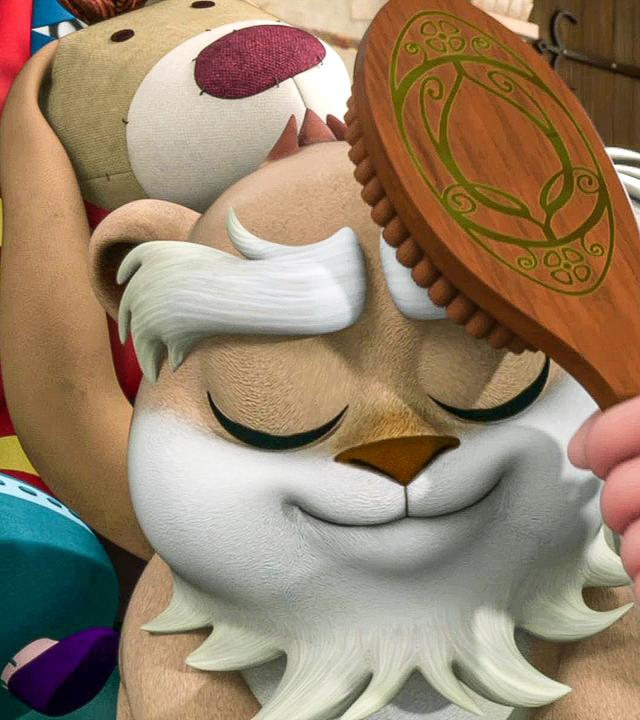 Der Hamster wird mit einer Bürste gebürstet. Er scheint es zu genießen. Im Hintergrund sind viele Kuscheltiere zu sehen.