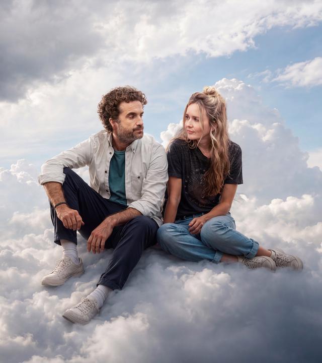 Markus und Miriam Bachmann (Oliver Wnuk, Stefanie Stappenbeck) sitzen einander zugewandt auf einer Wolke. Links neben ihnen zieht ein Gewitter heran, es blitzt.