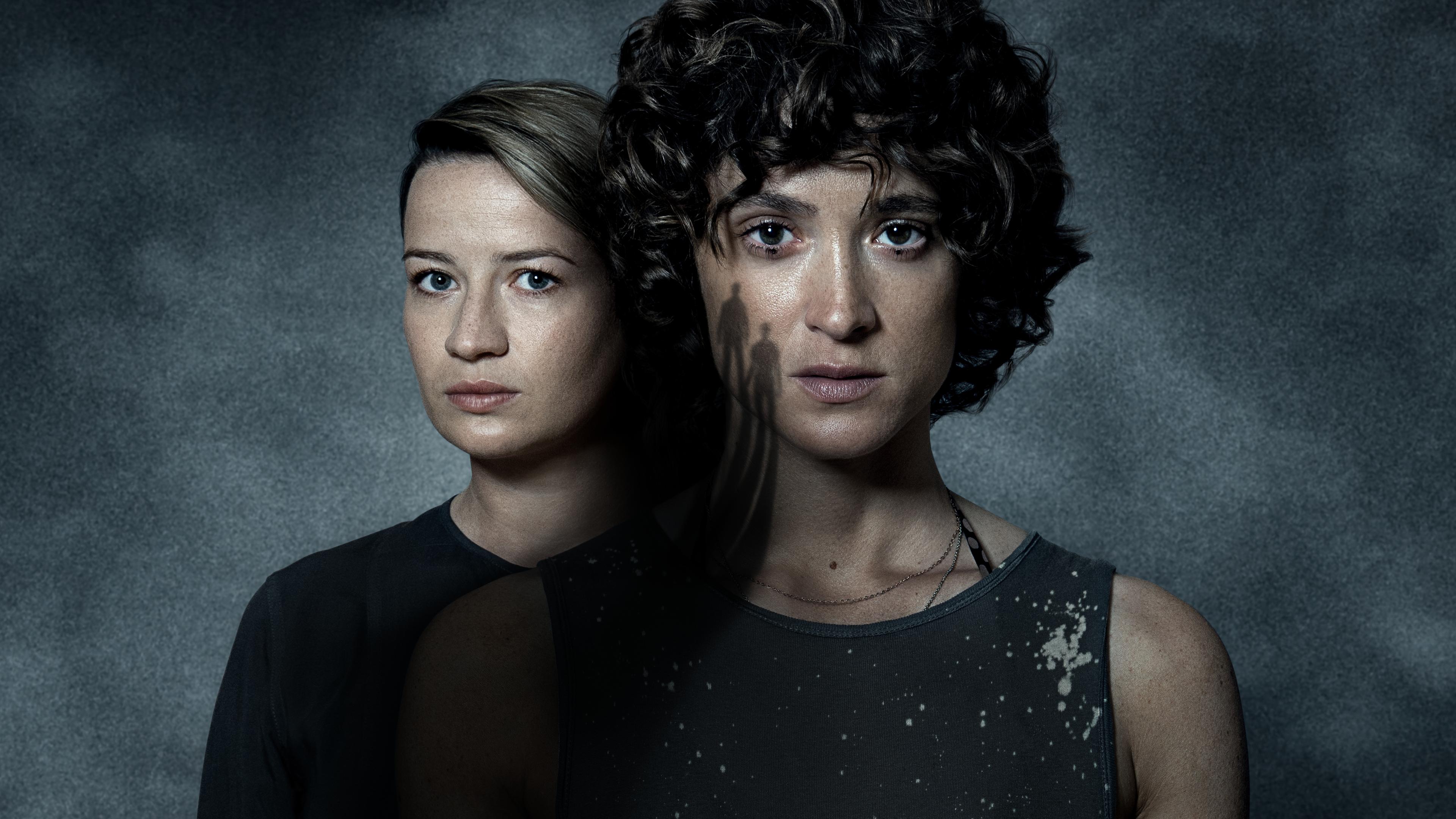 Die Schauspielerinnen Nina Gummich und Friederike Beckt stehen halb versetzt hintereinander und blicken ernst in die Kamera.